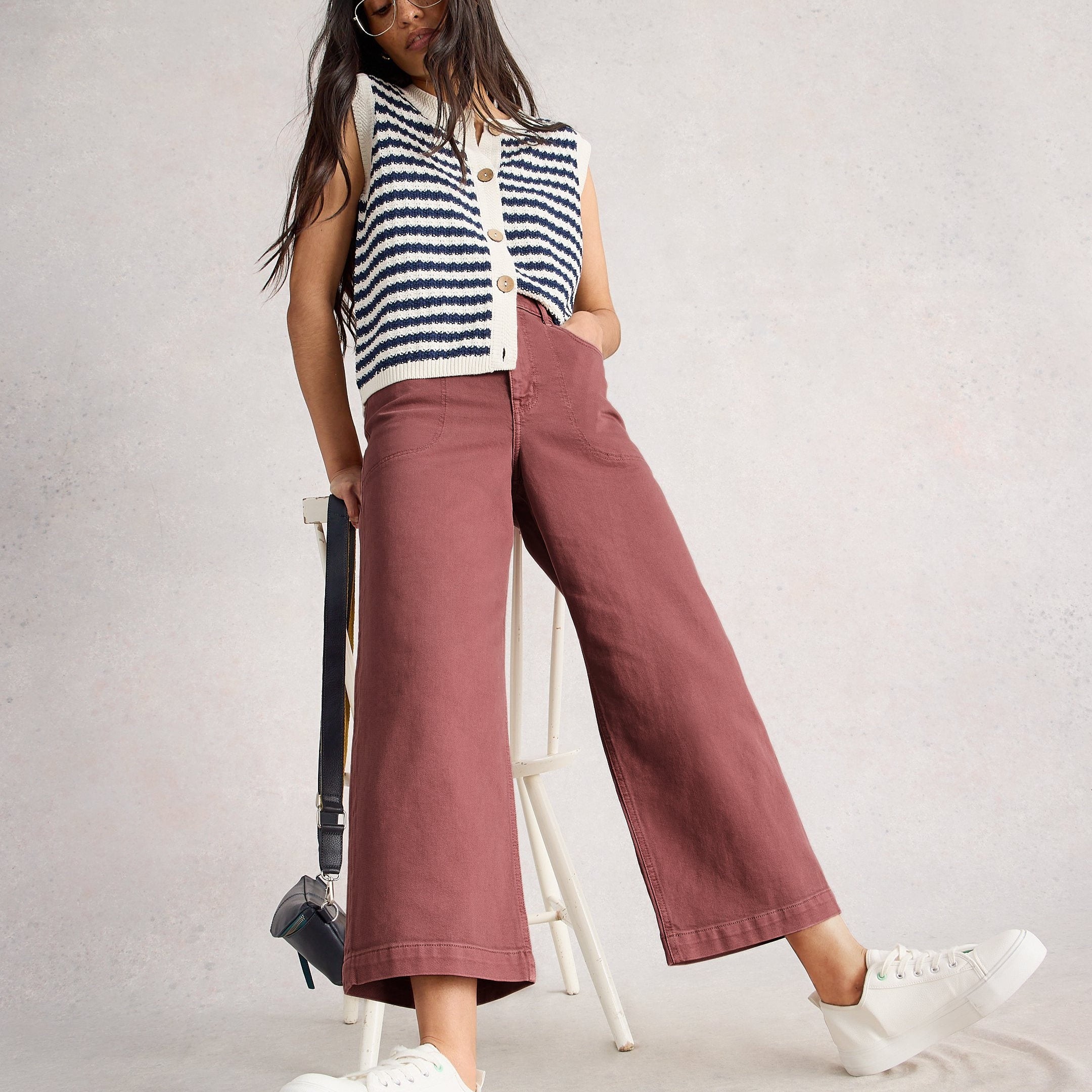Woman wearing a striped sleeveless top and wide-leg pants on a plain background