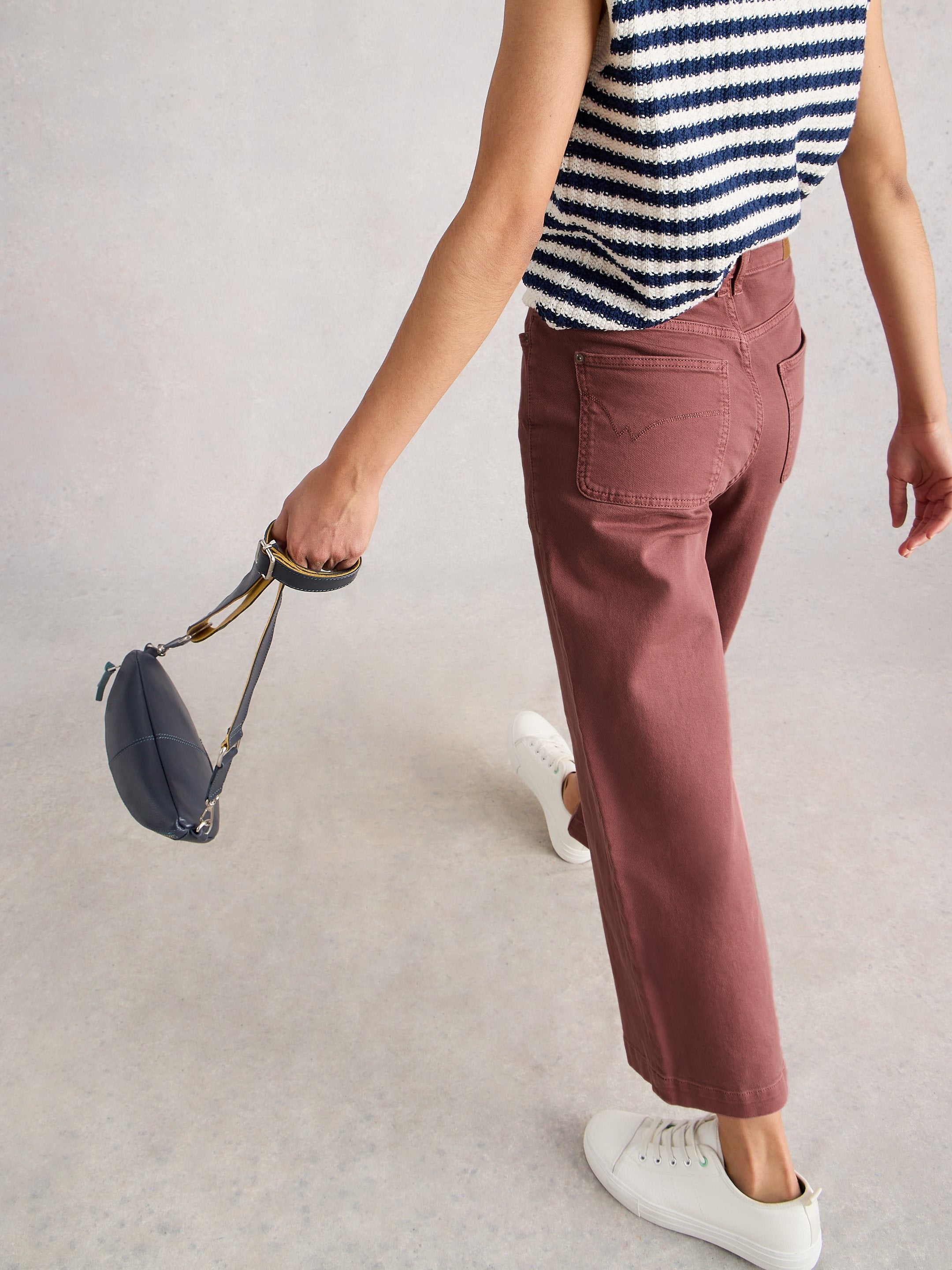 Person wearing a striped shirt and pink pants, holding a small bag on a light gray background