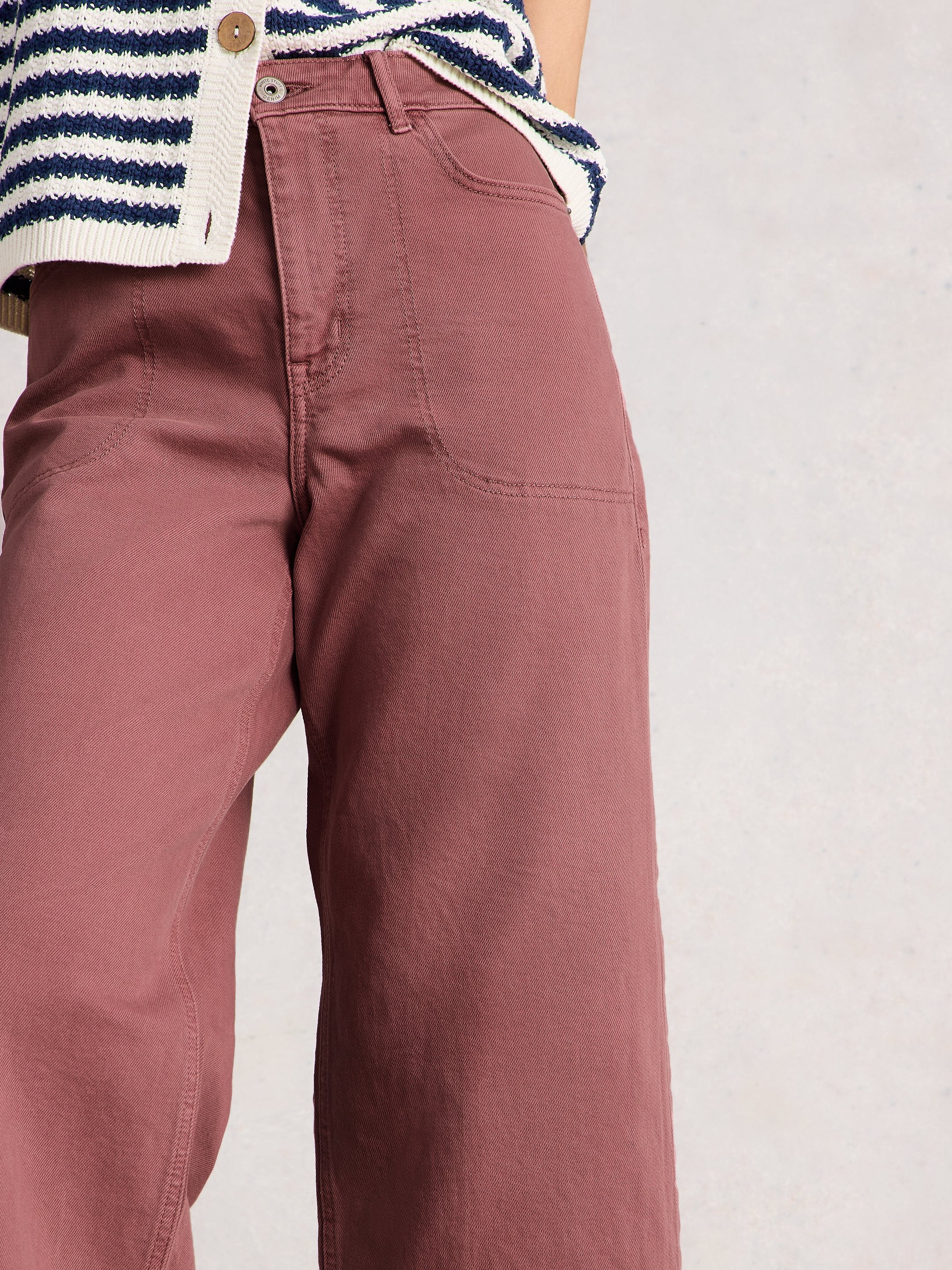 Maroon pants worn with a striped sweater on a plain background