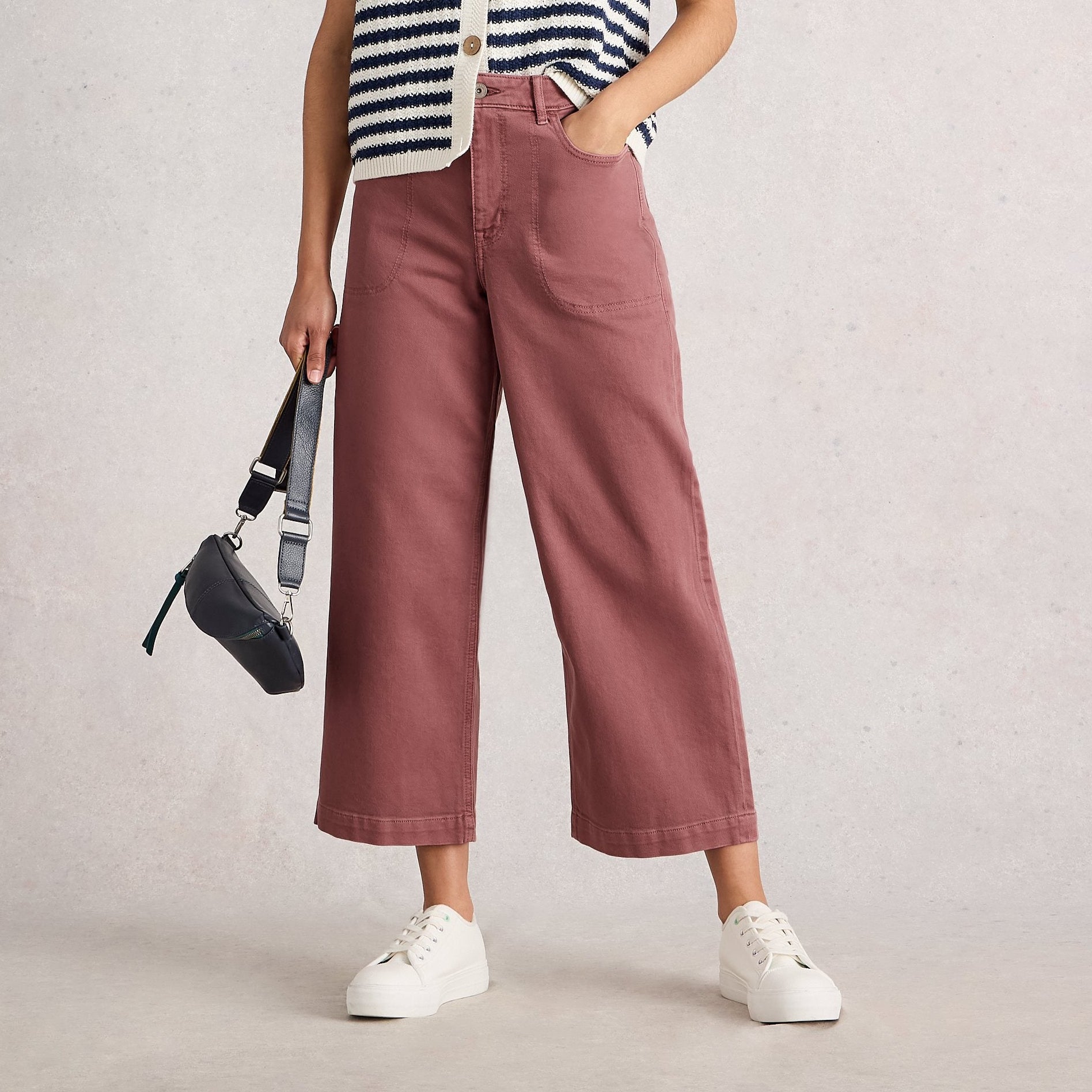 Woman wearing a striped sleeveless top and pink pants, holding a black bag on a plain background