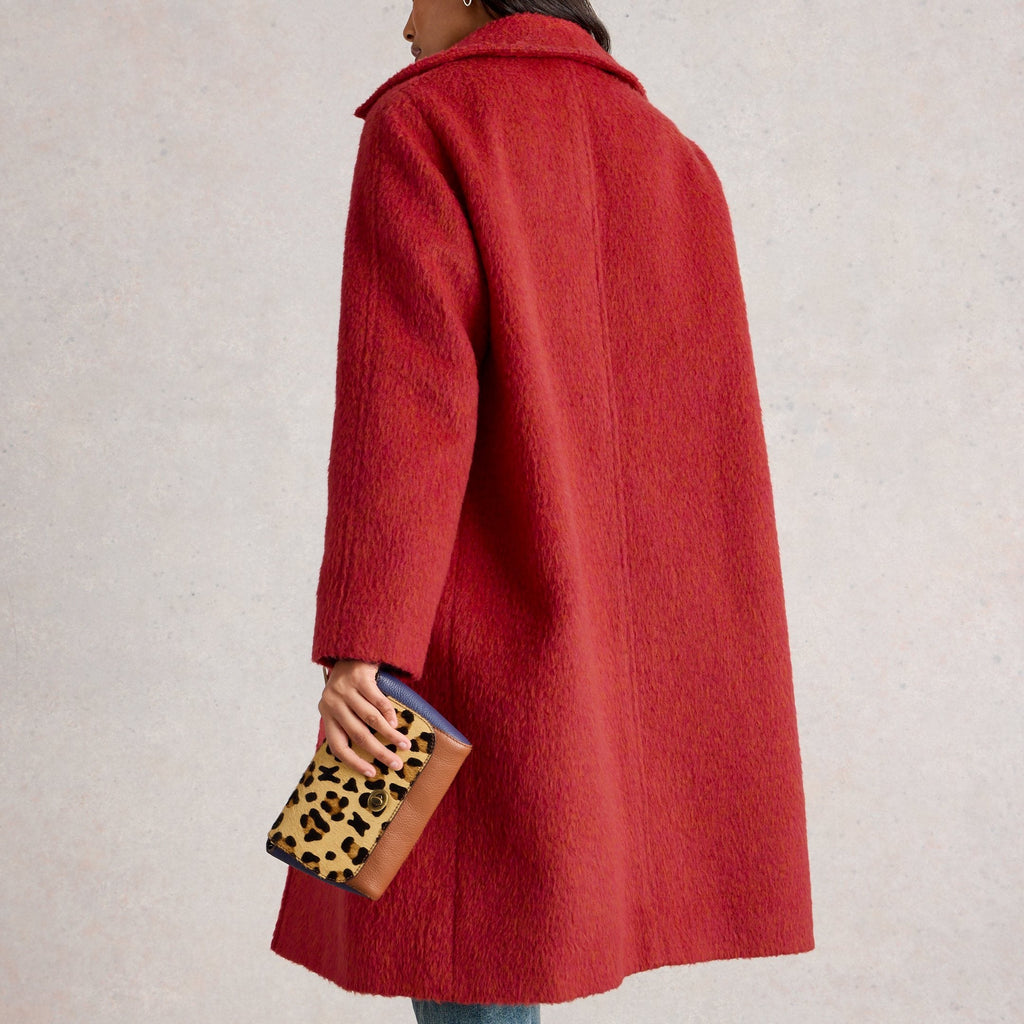 Person wearing a red coat holding a clutch with a leopard print design on a plain background