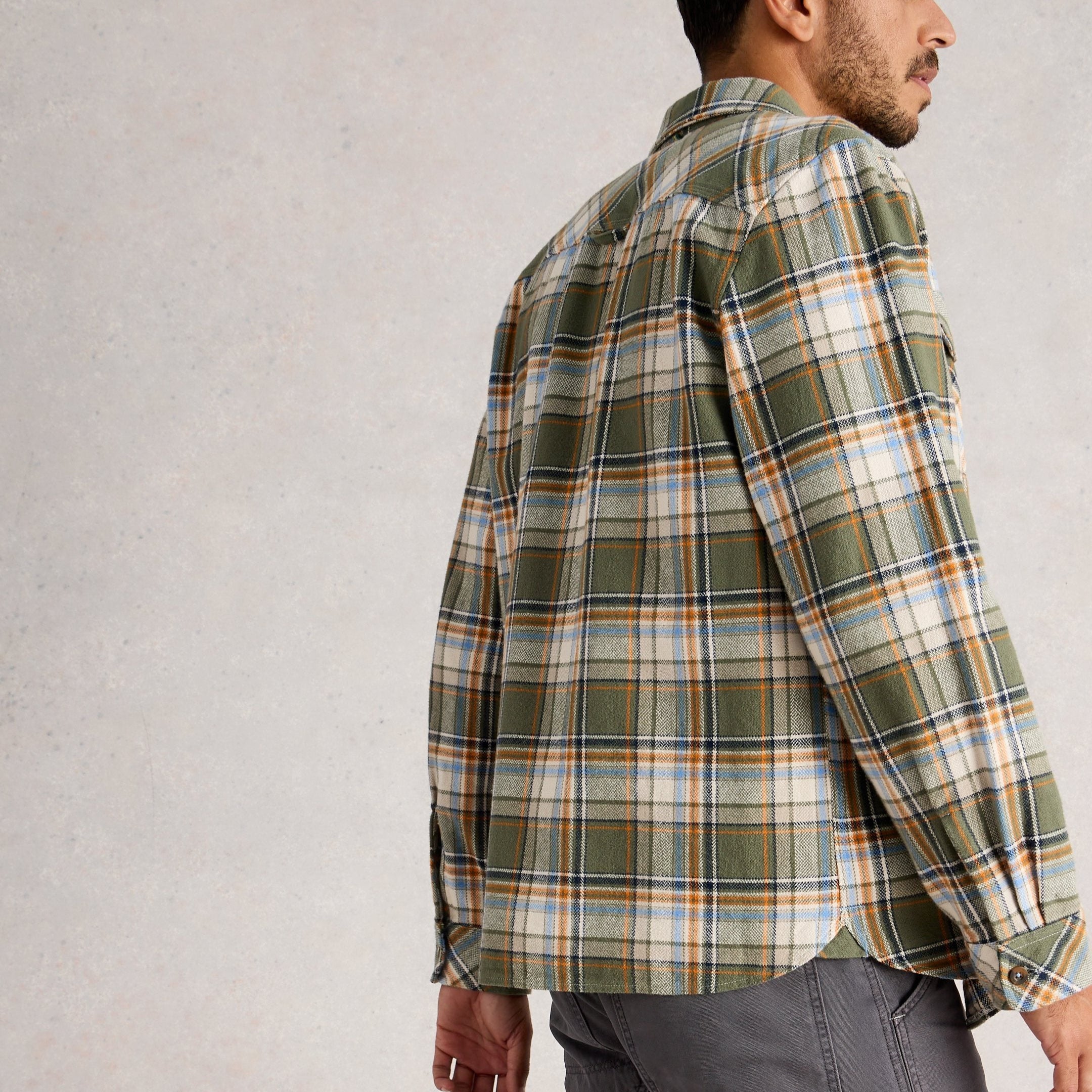 Man wearing a green plaid shirt and gray pants on a light gray background