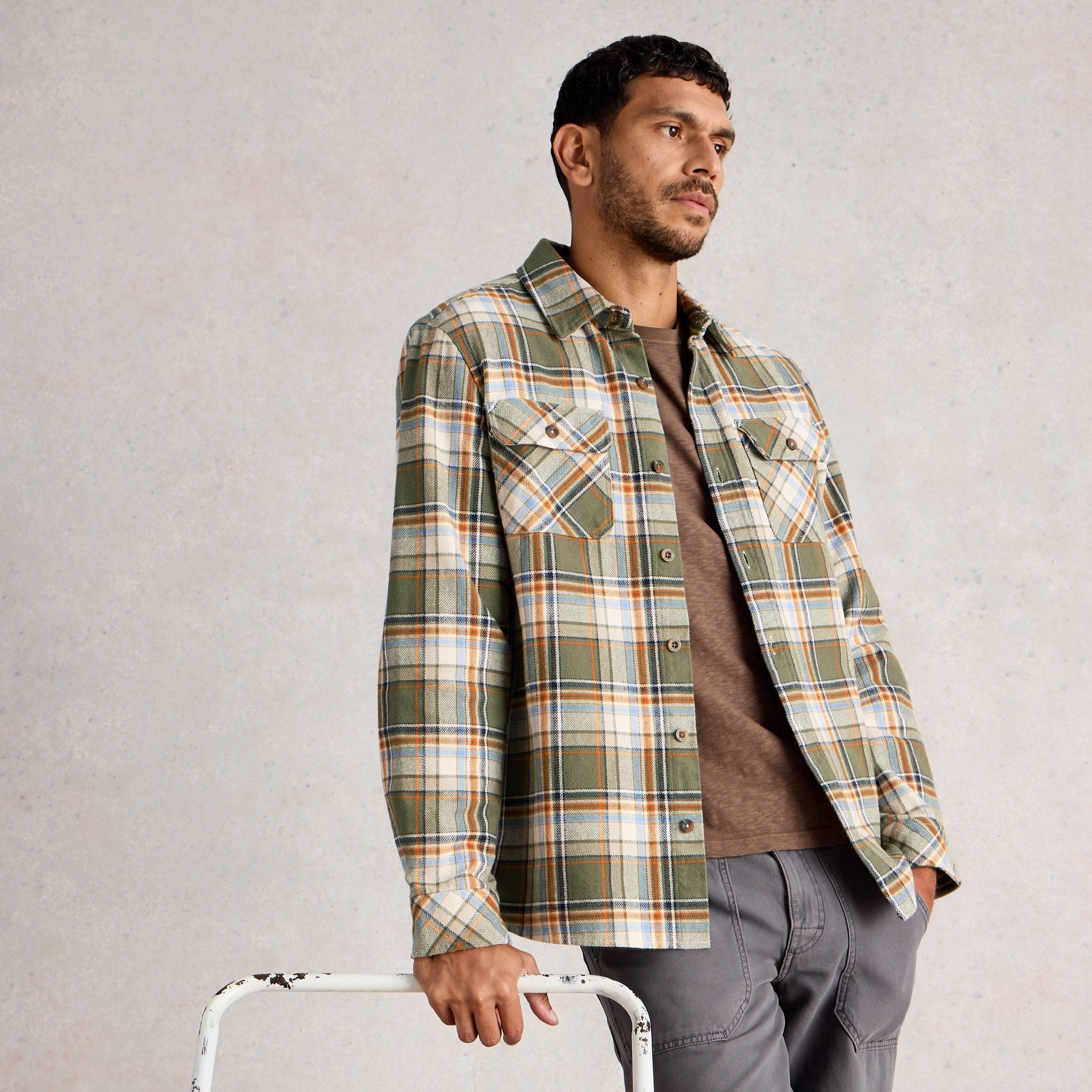 Man wearing a plaid shirt and holding a white chair with wooden accents against a plain background