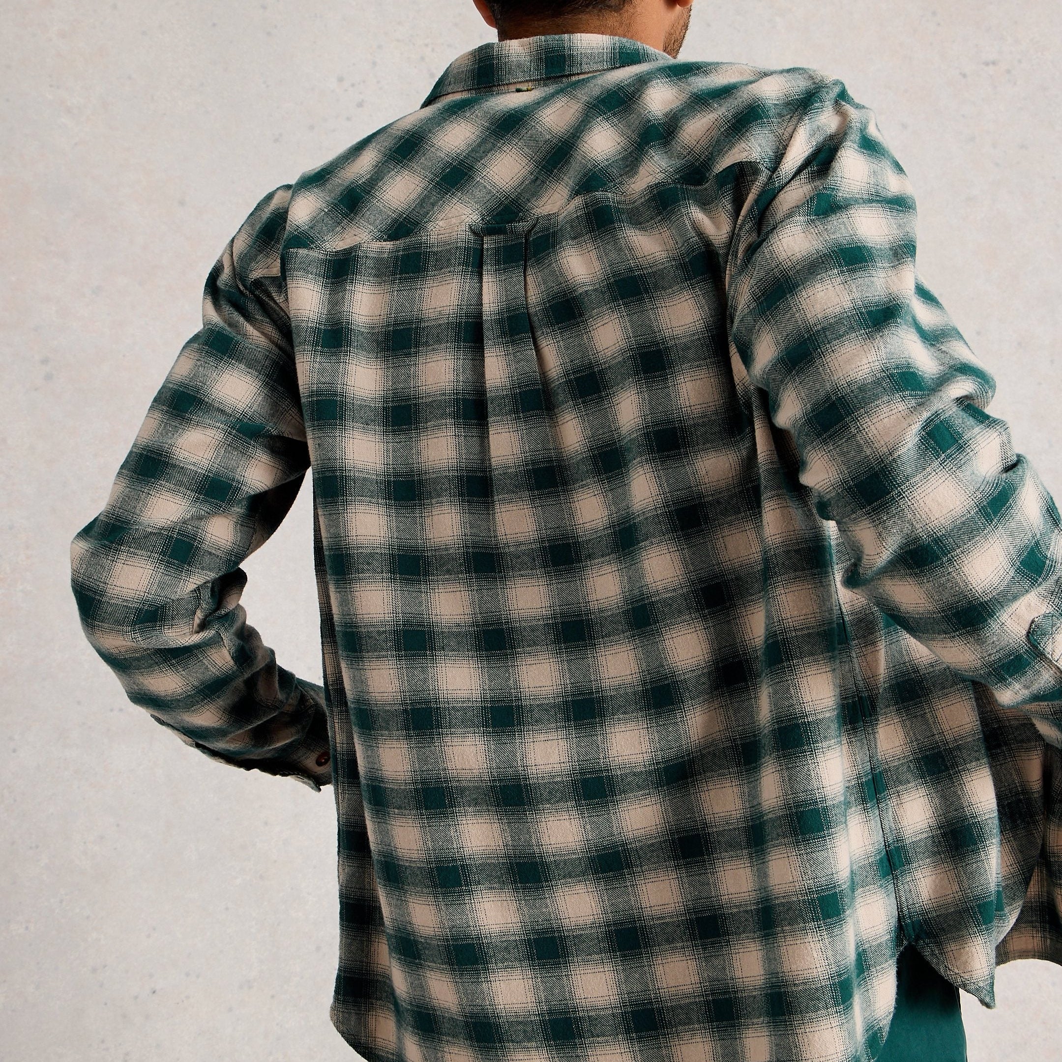 Person wearing a green and beige checkered shirt against a plain background