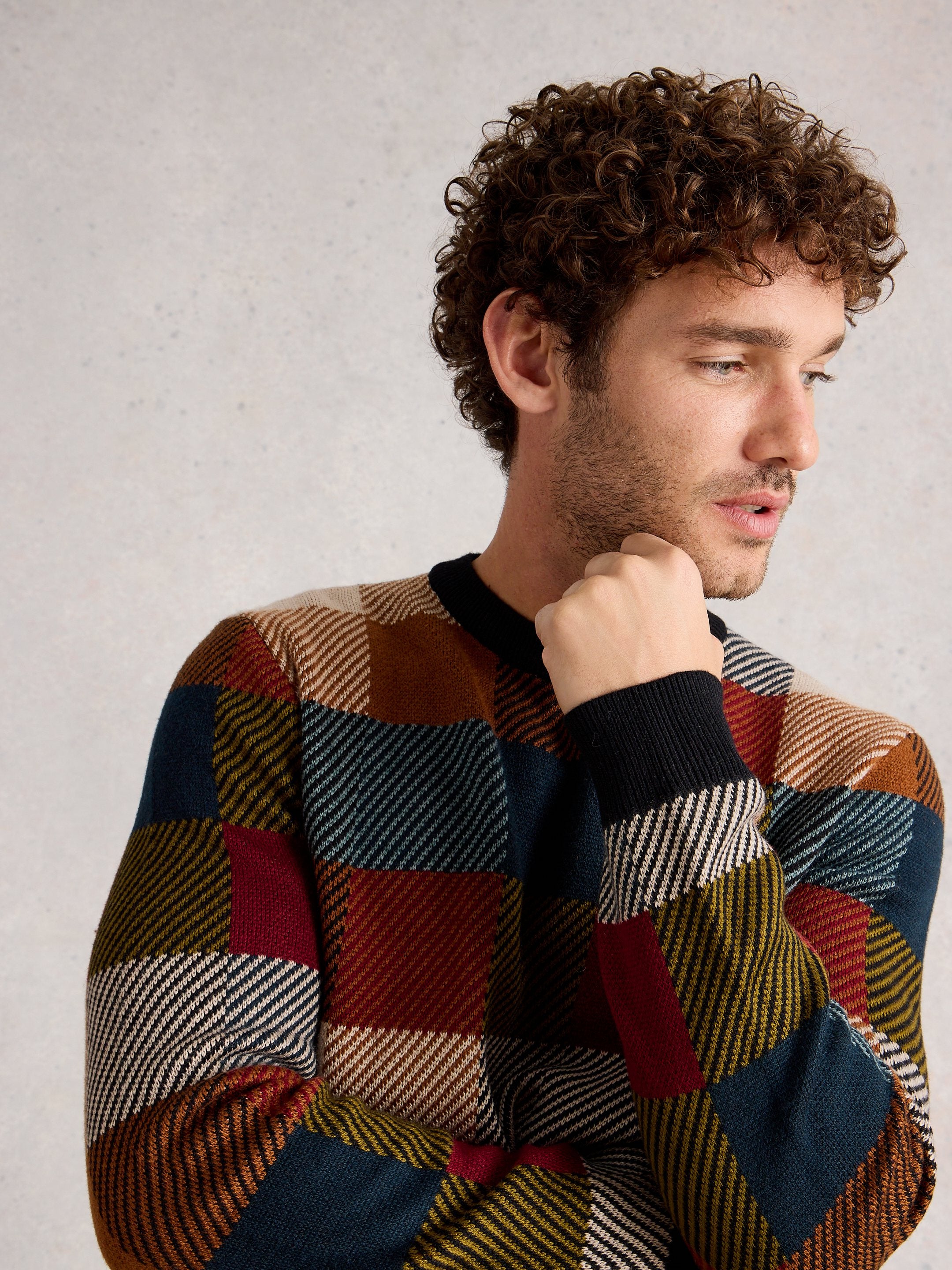 Man wearing a colorful checkered sweater against a neutral background