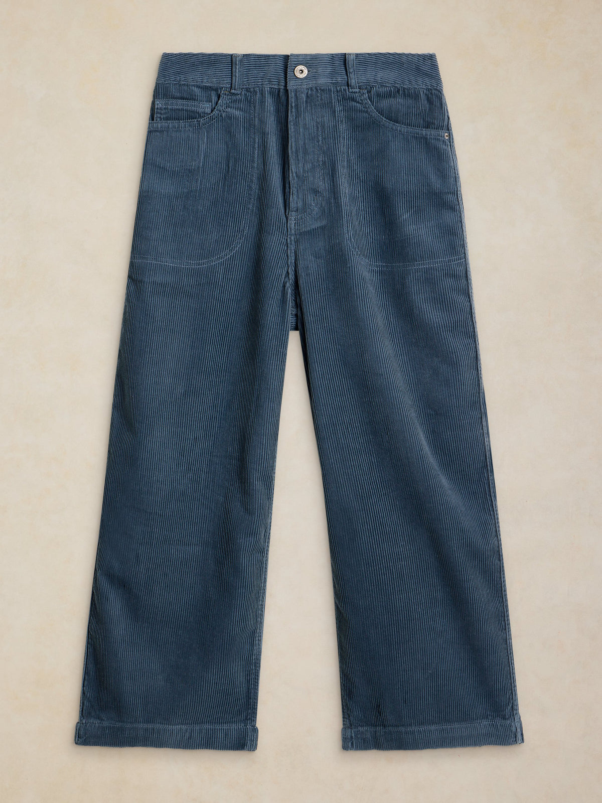 A pair of dark blue corduroy trousers laid flat on a light beige textured background.