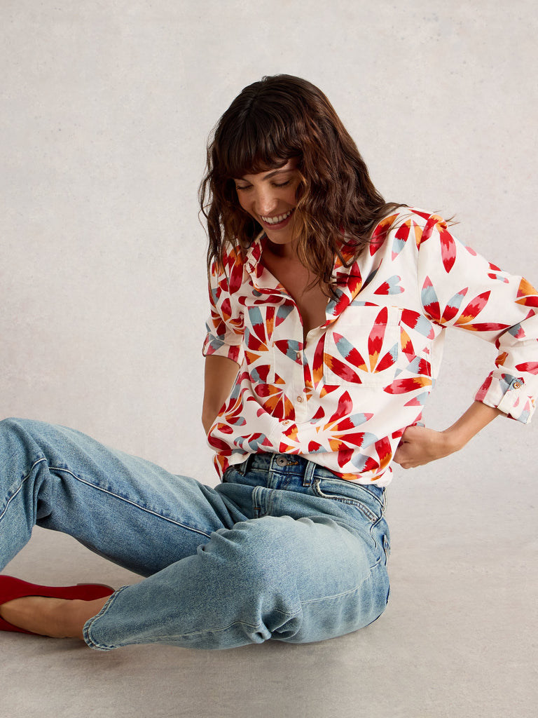 Woman wearing a colorful geometric patterned shirt and blue jeans sitting on the floor.