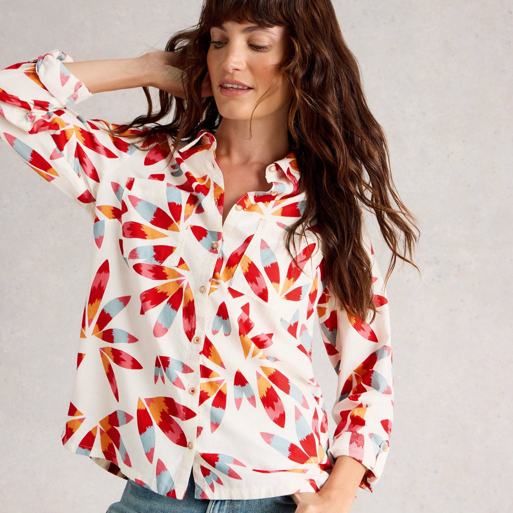 Woman wearing a colorful patterned blouse and jeans against a plain background