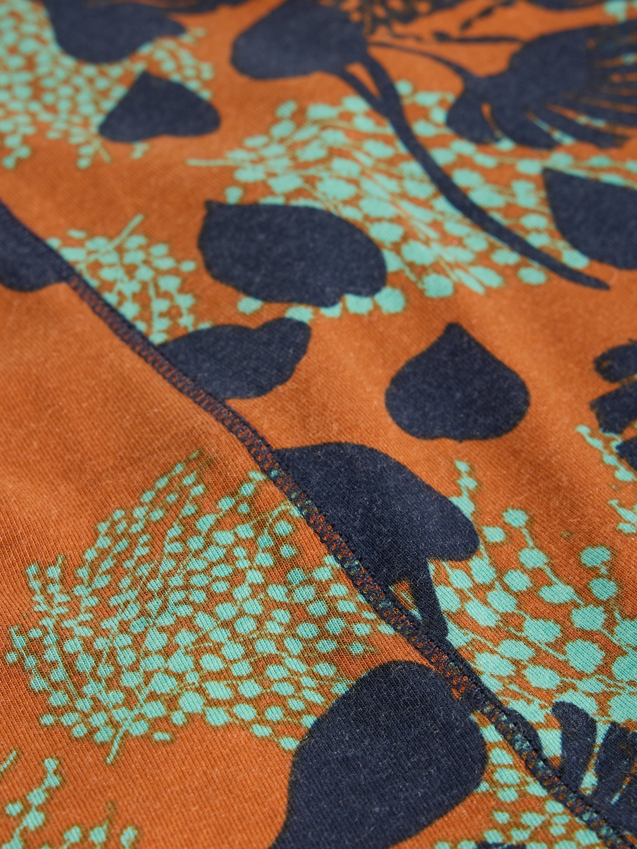 Close-up of fabric with orange background and black and green leaf pattern