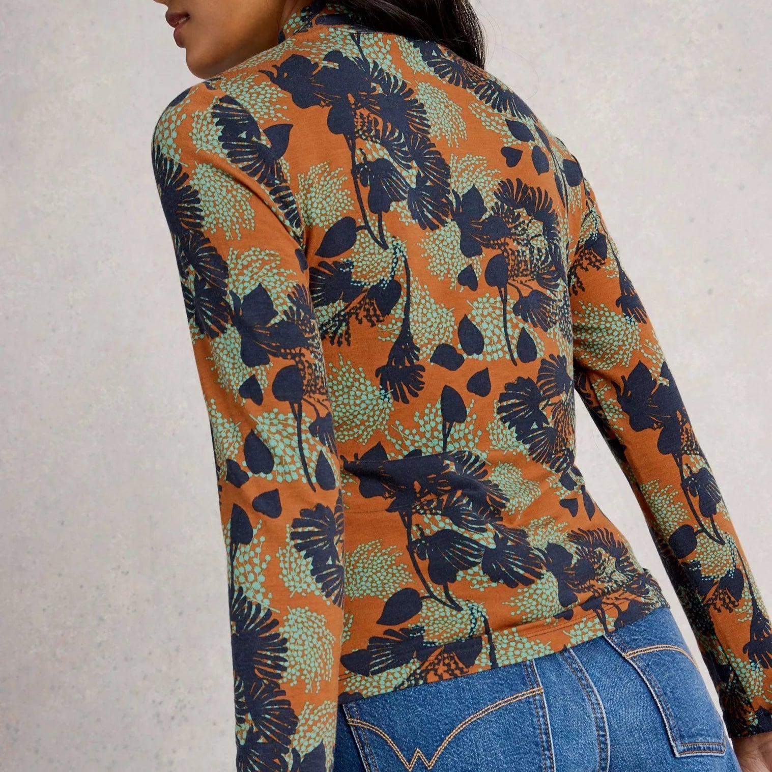 Person wearing a colorful floral shirt and blue jeans against a neutral background