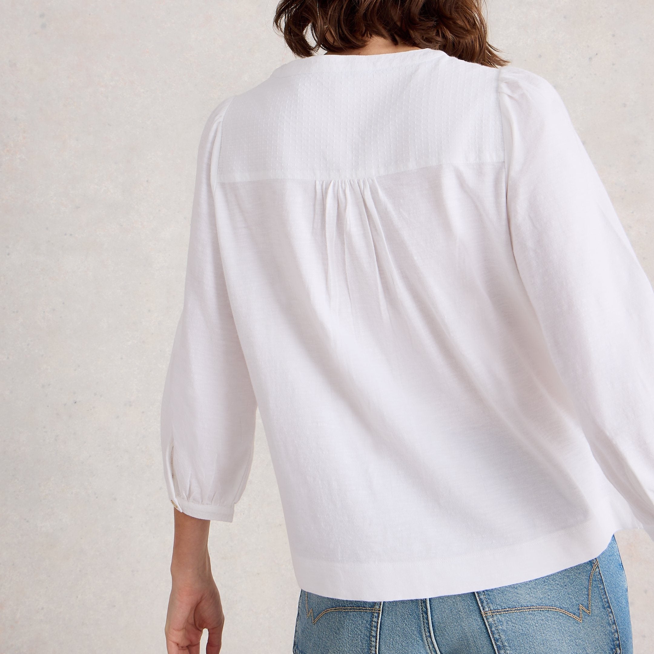 Person wearing a white blouse and blue jeans against a plain background