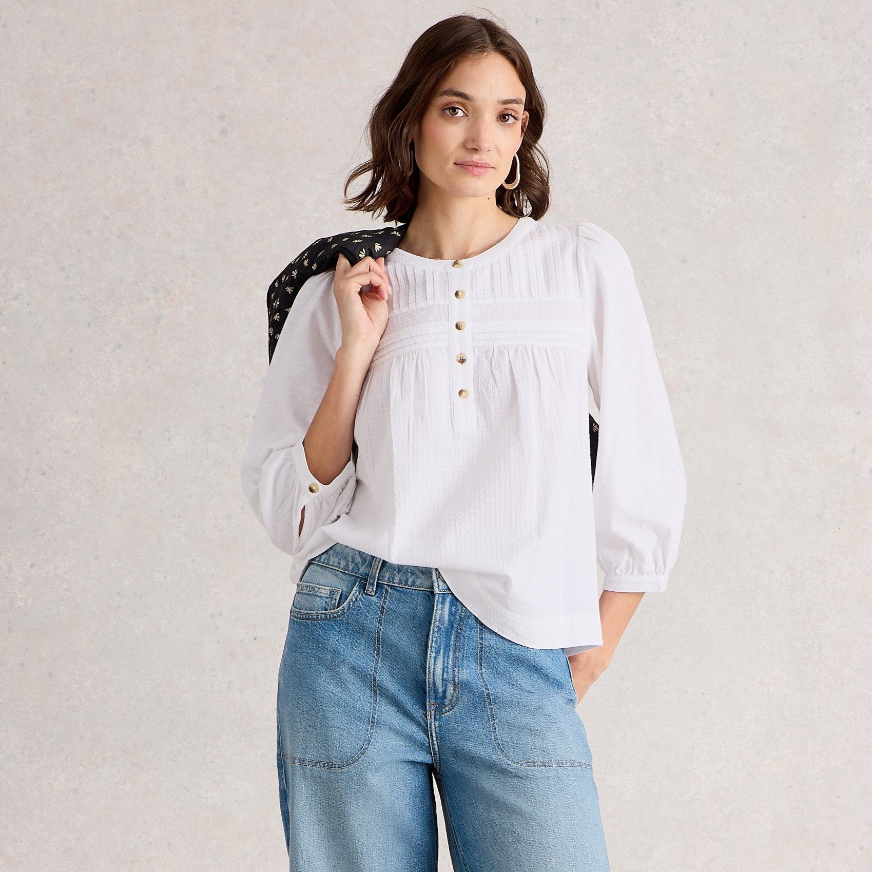Woman wearing a white blouse and blue jeans against a plain background