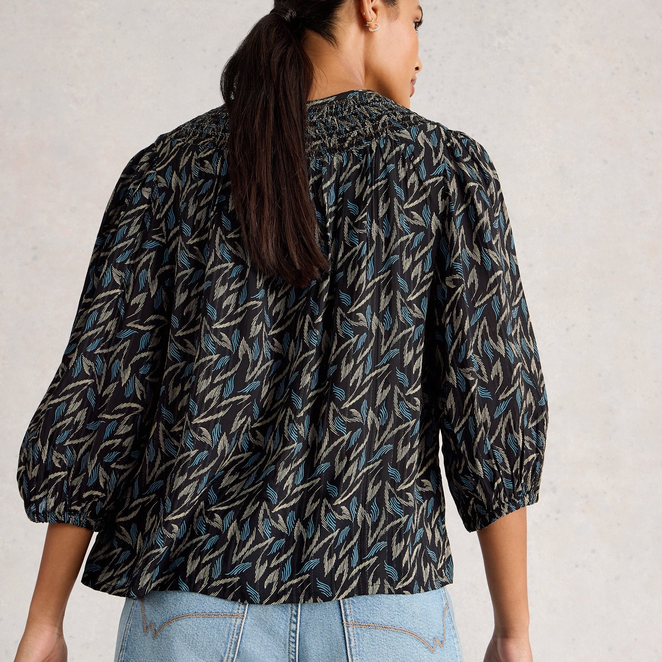 Person wearing a patterned shirt and jeans against a neutral background