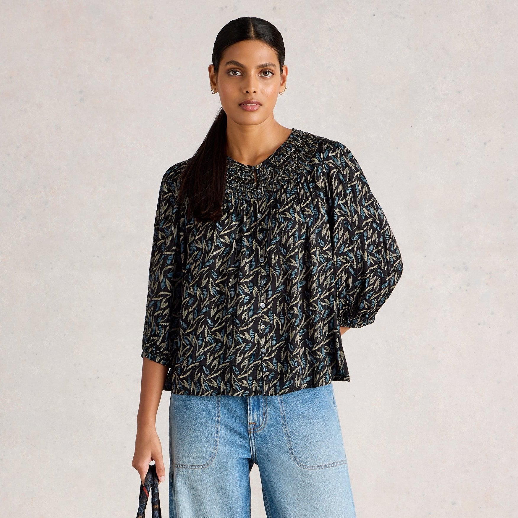 Woman wearing a patterned blouse and jeans against a plain background