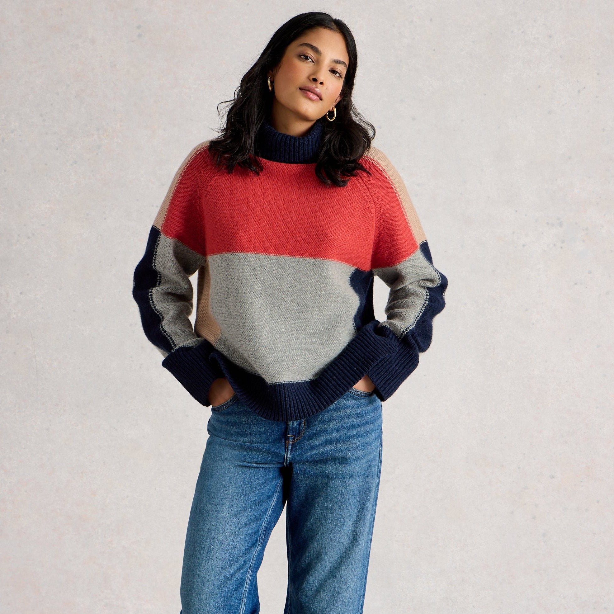 Woman wearing a colorful sweater and blue jeans against a plain background