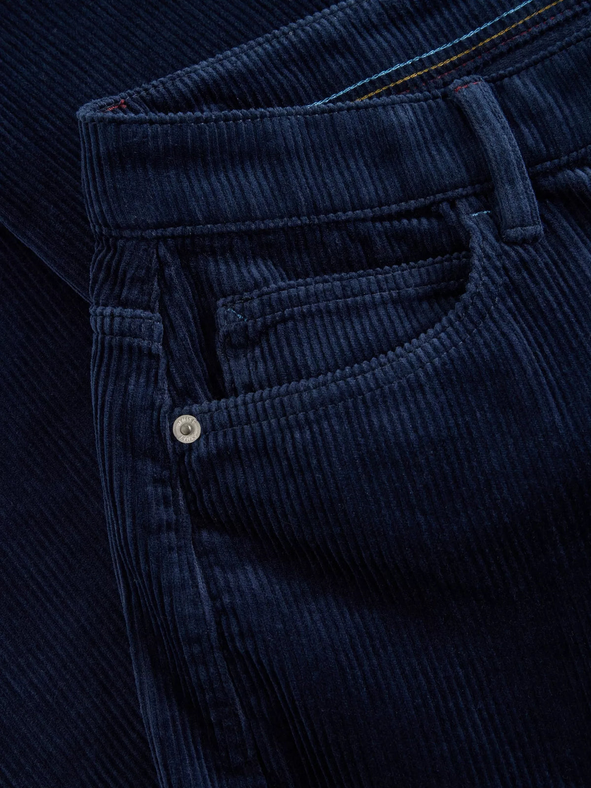 Close-up of dark navy blue corduroy pants showing the front pocket, button, and ribbed fabric texture.