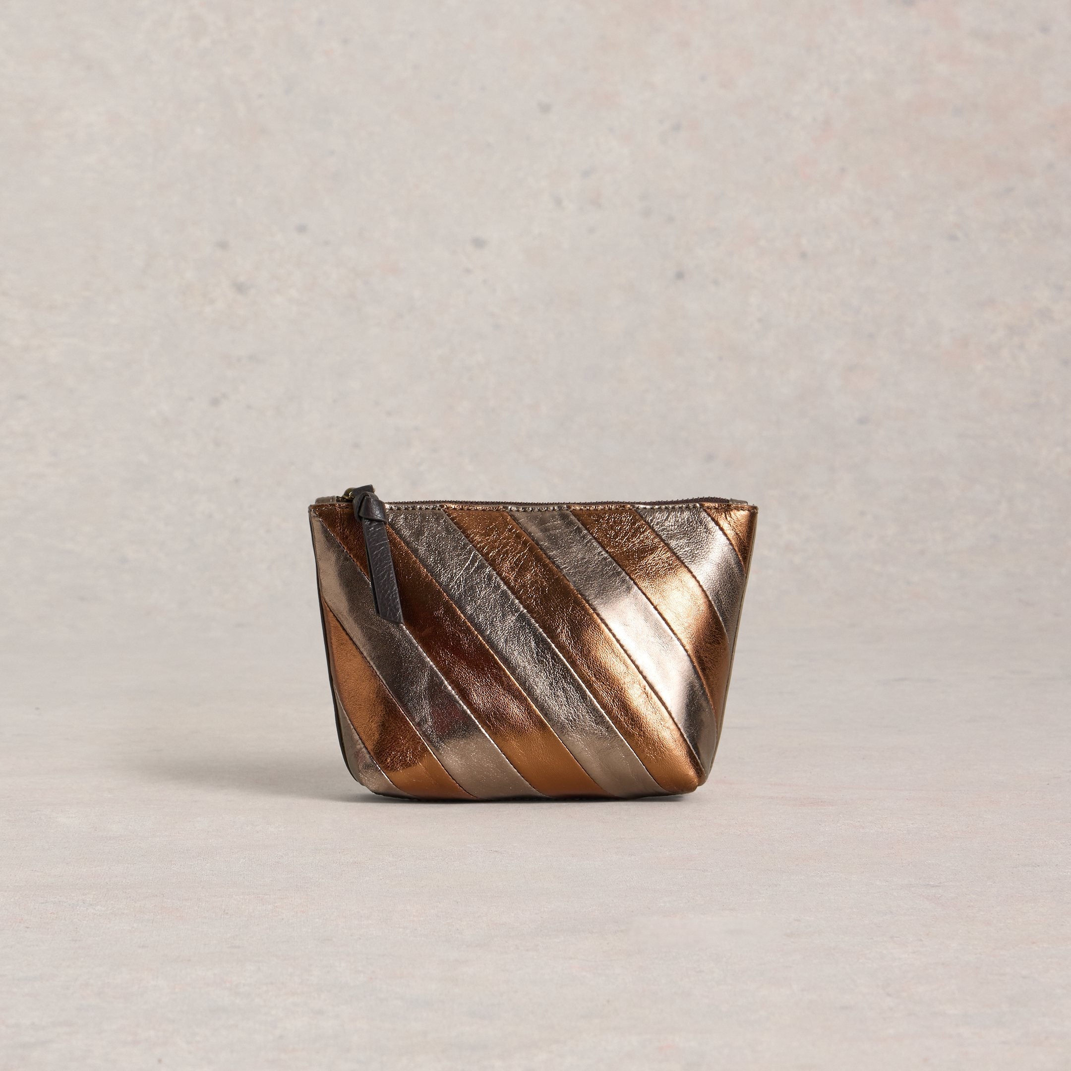Metallic pouch with diagonal stripes on a beige background