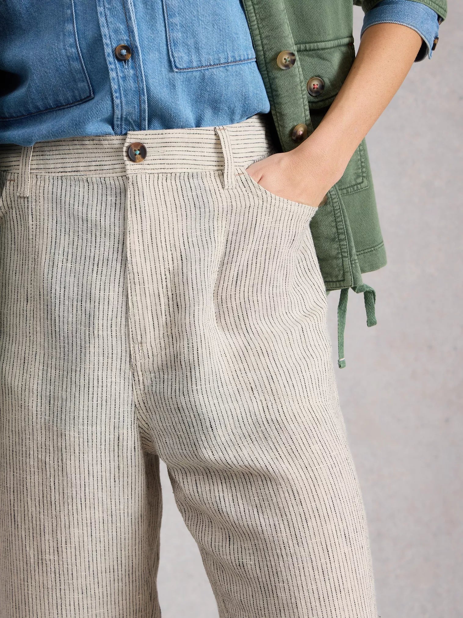 Person wearing beige corduroy pants with a blue shirt and green vest on a gray background