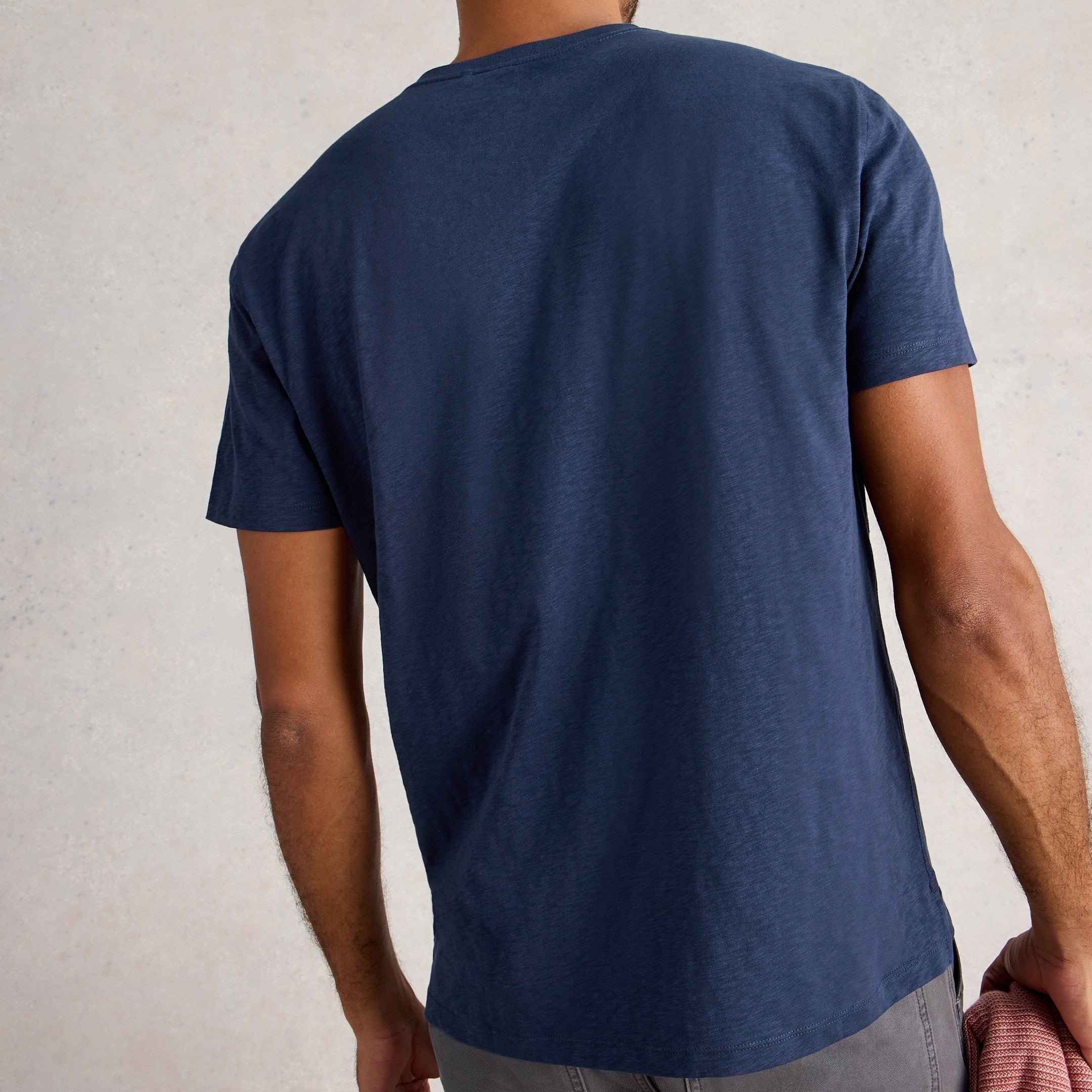 Man wearing a blue t-shirt and gray pants against a plain background