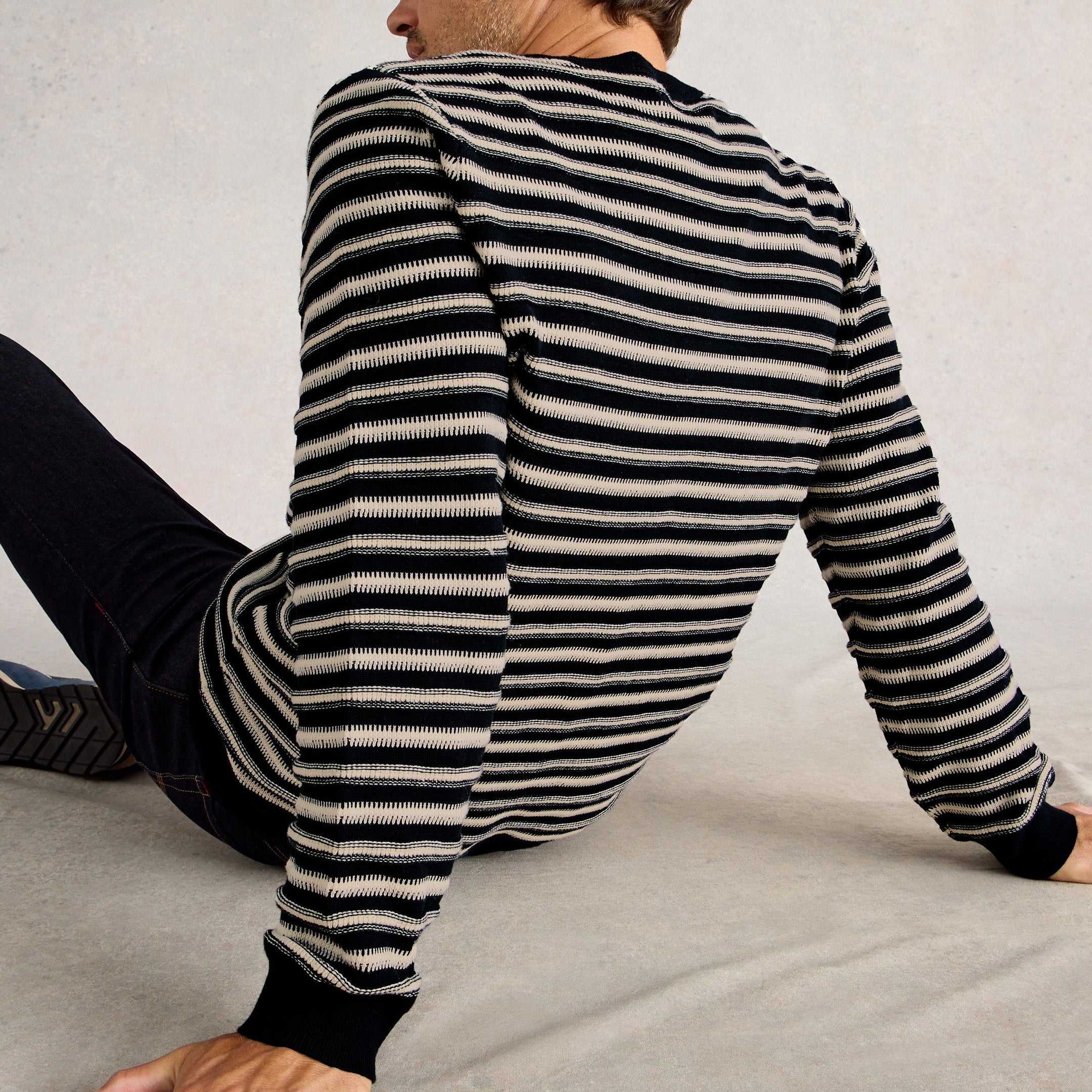 Person wearing a black and white striped sweater sitting on a gray surface.