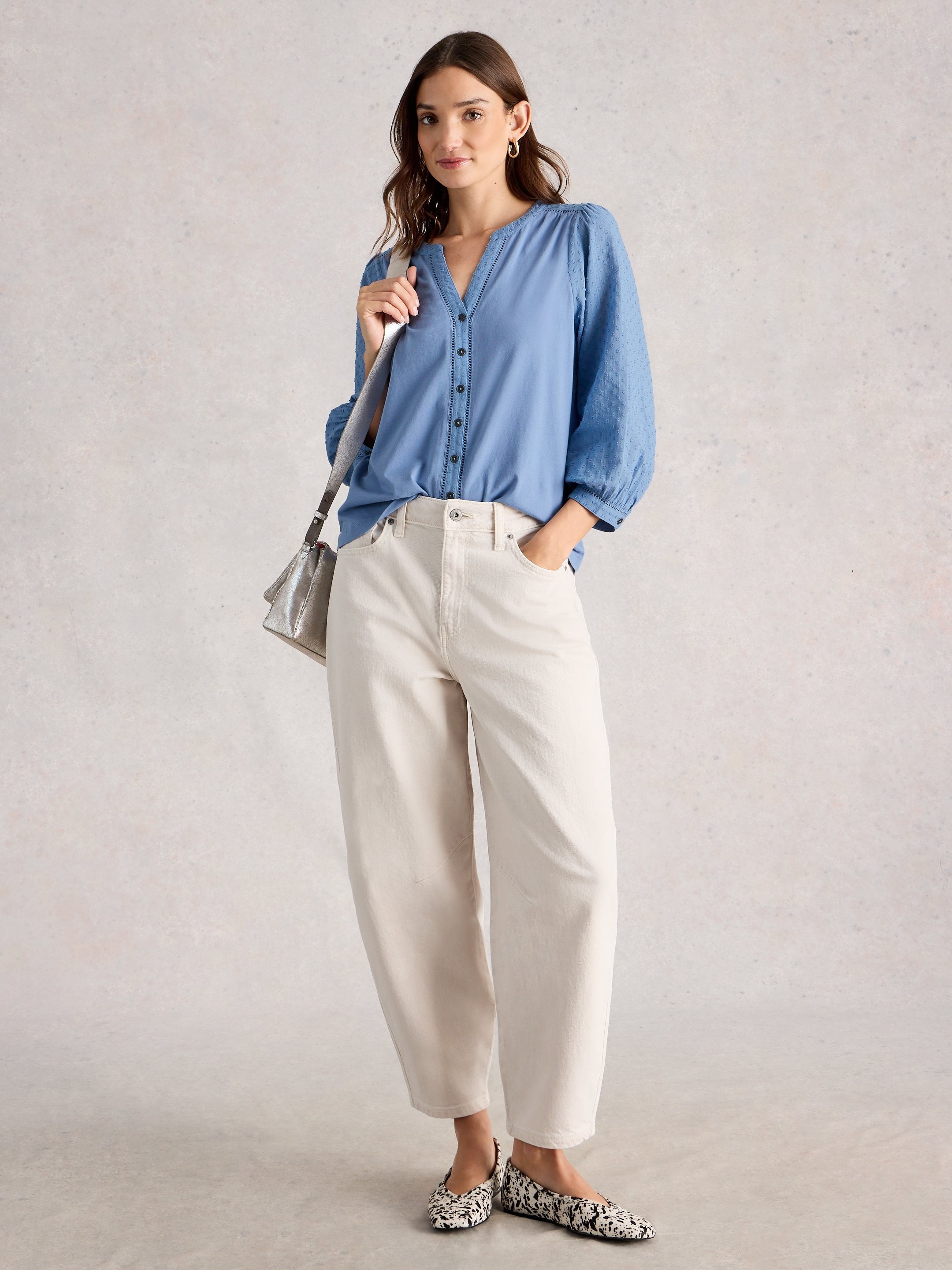 Woman wearing a blue shirt and white pants with a gray background