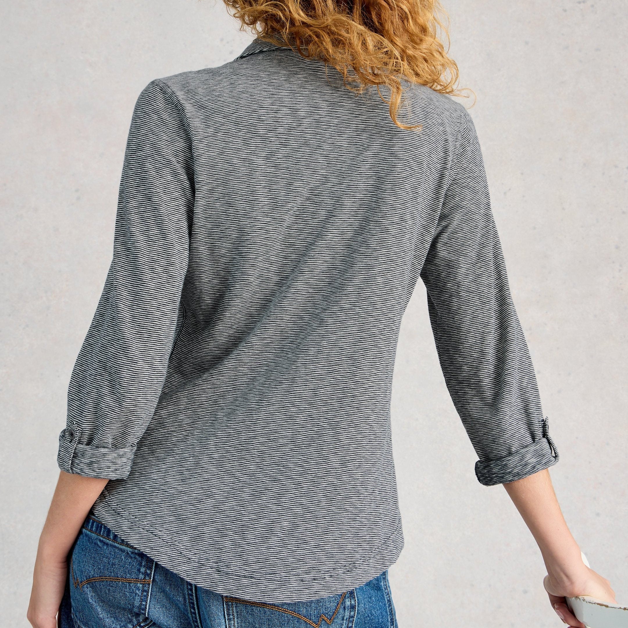 Person wearing a gray button-up shirt and blue jeans against a light gray background