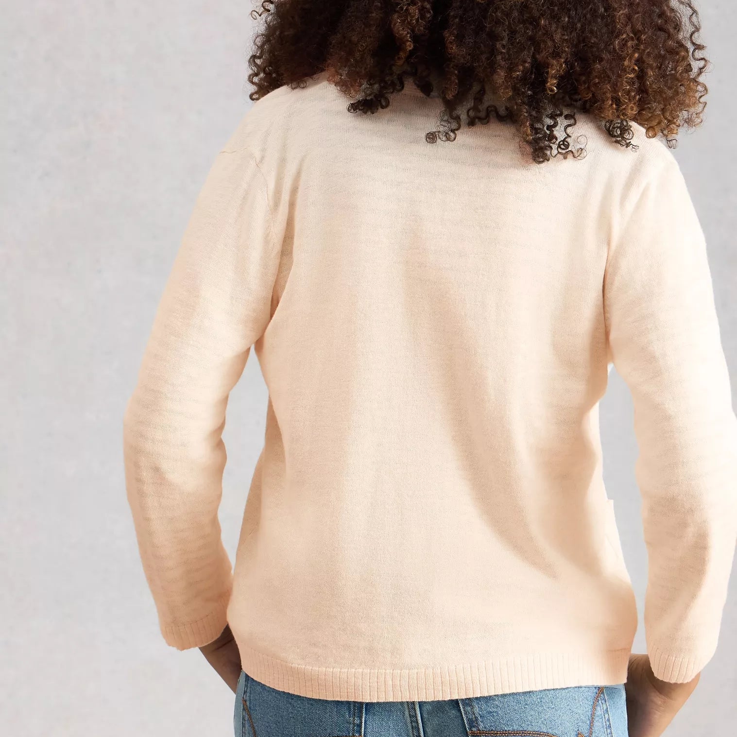 Person wearing a beige sweater and blue jeans against a plain background