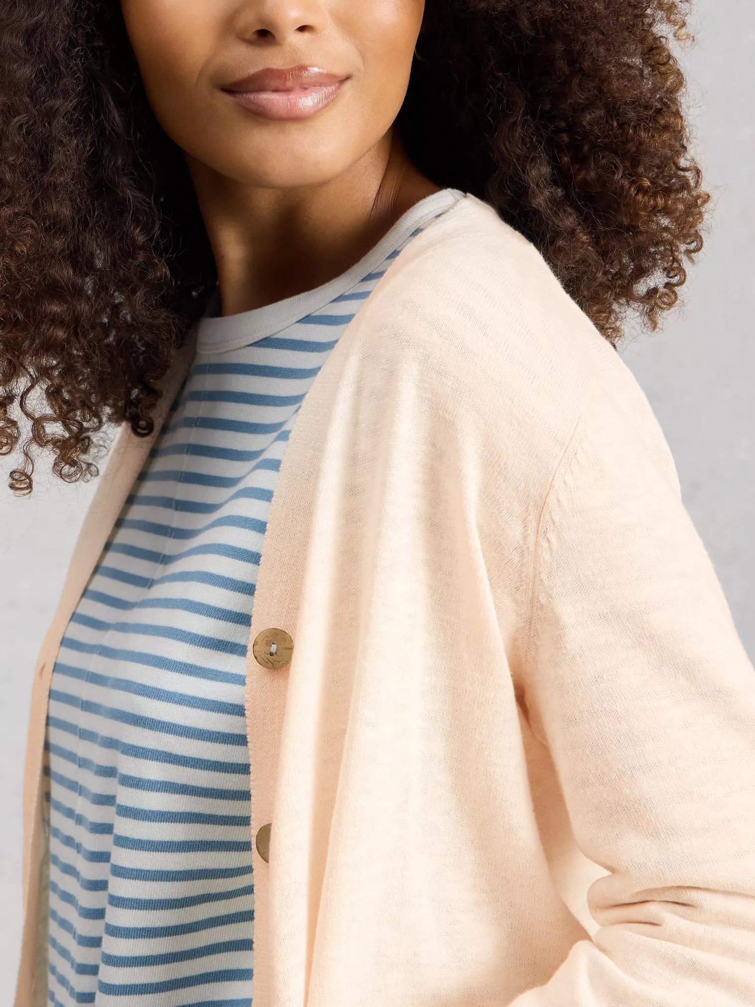 Woman wearing a beige cardigan over a blue and white striped shirt against a gray background