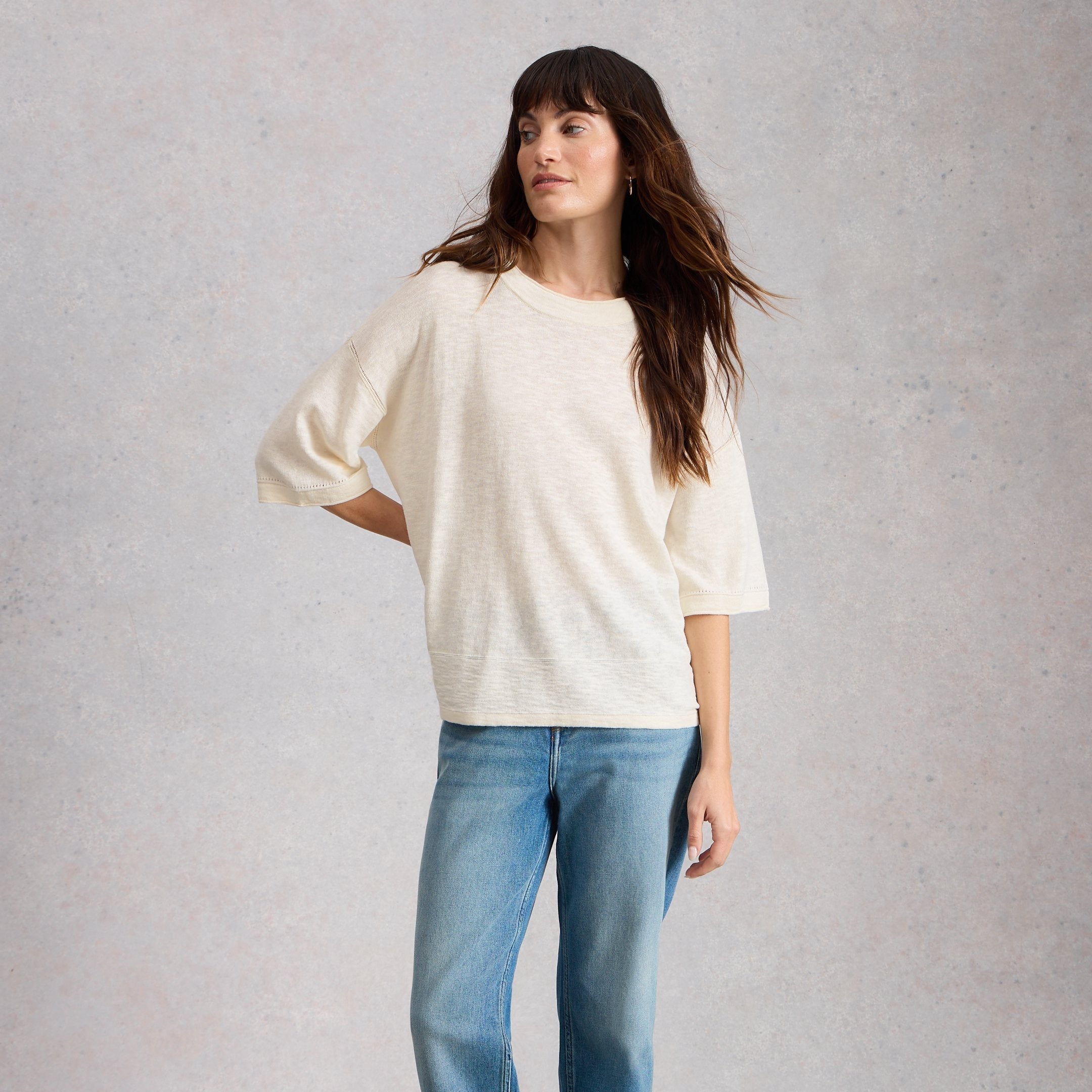 Woman wearing a white oversized sweater and blue jeans against a plain background