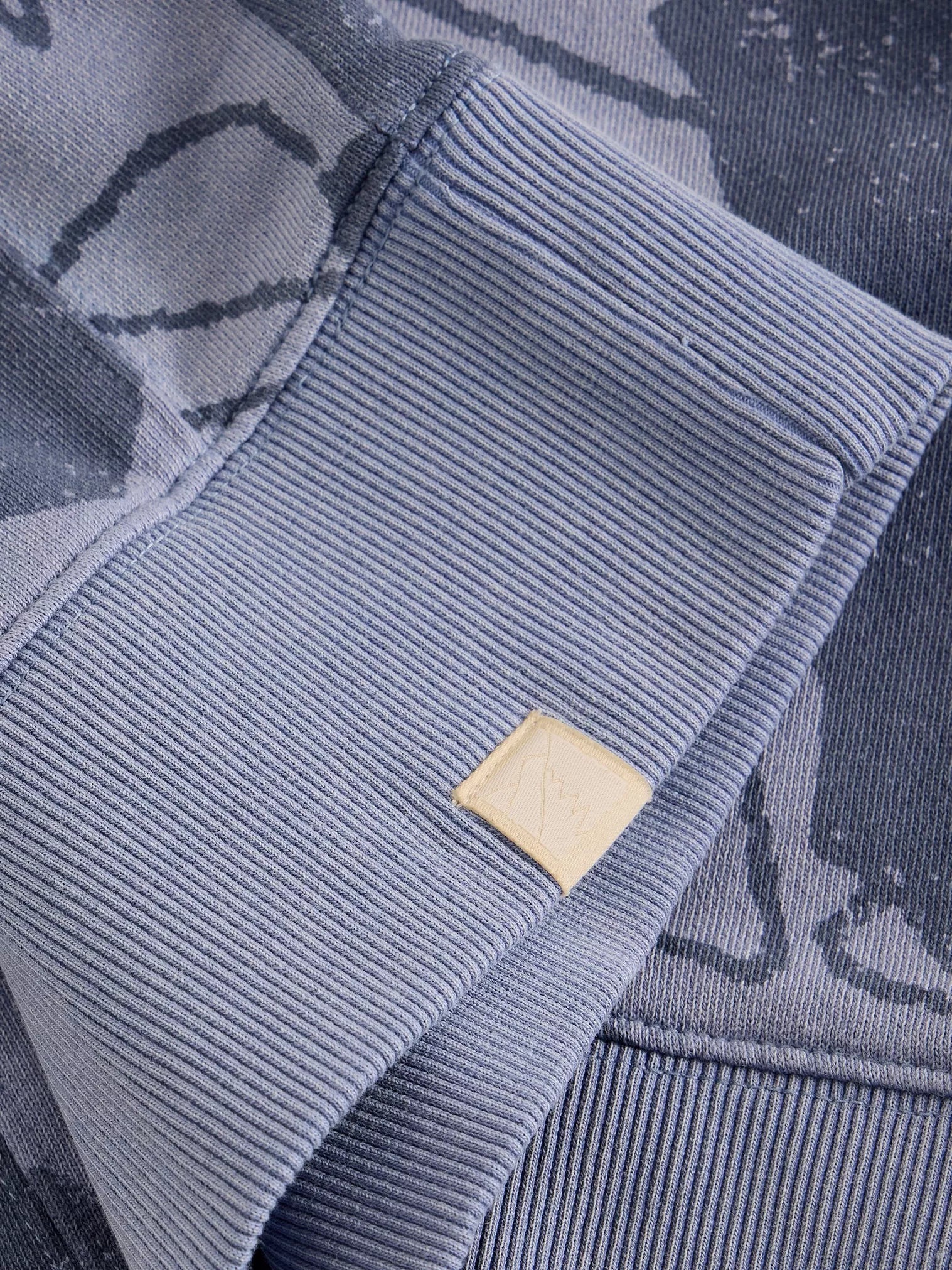 Close-up of a ribbed blue sweater with a brand label on a matching background
