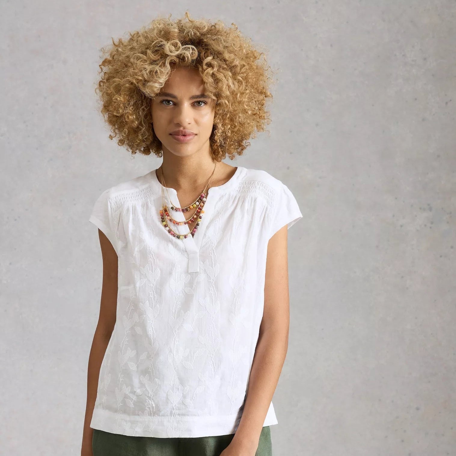 Woman wearing a white top and green shorts against a plain background