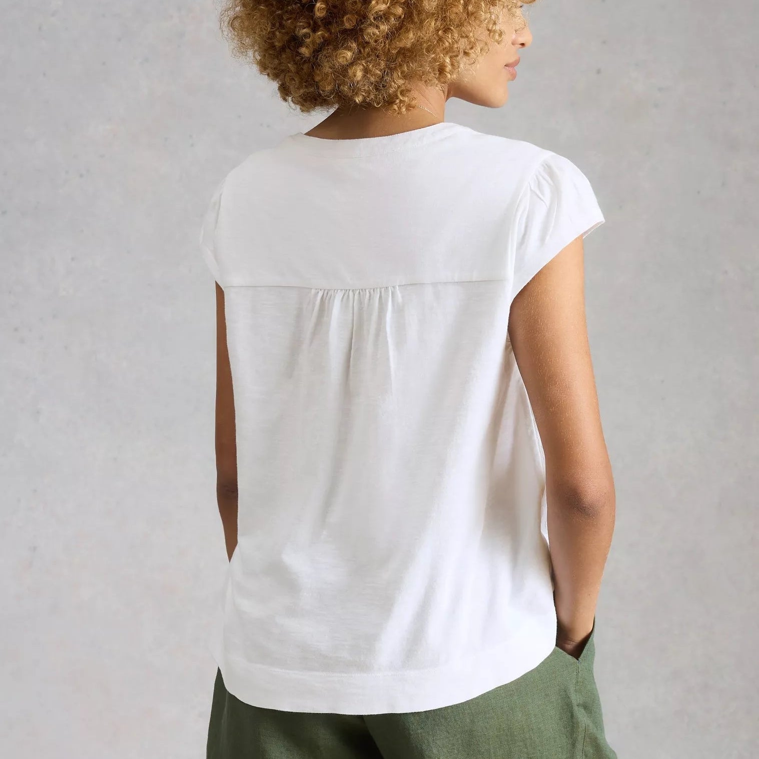 Person wearing a white sleeveless top with green pants against a plain background