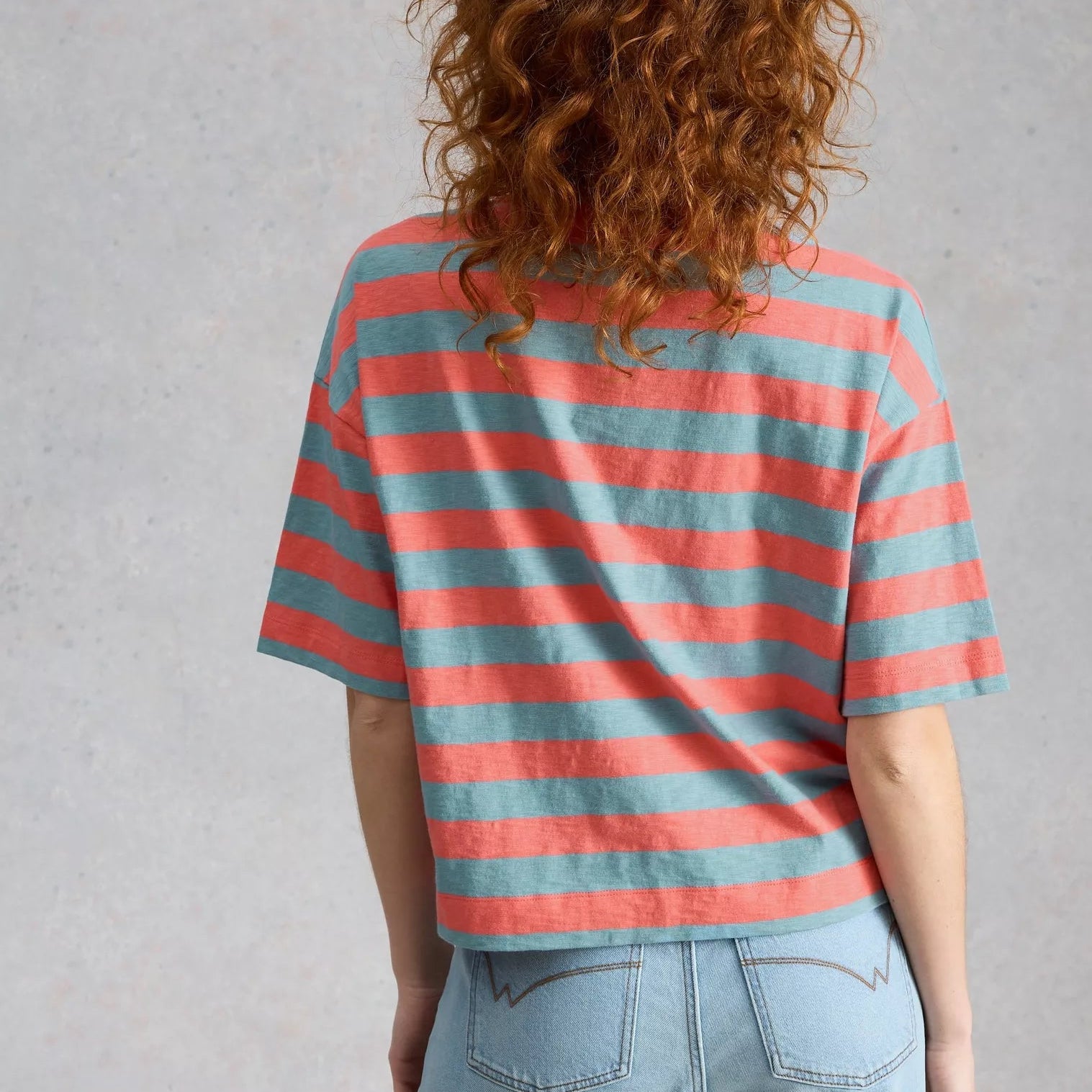 Person wearing a striped shirt and jeans against a plain background