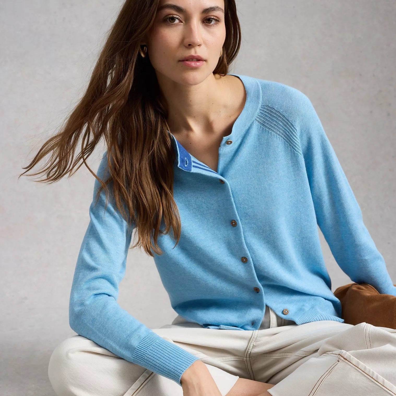 Woman wearing a light blue cardigan sitting on the floor against a neutral background