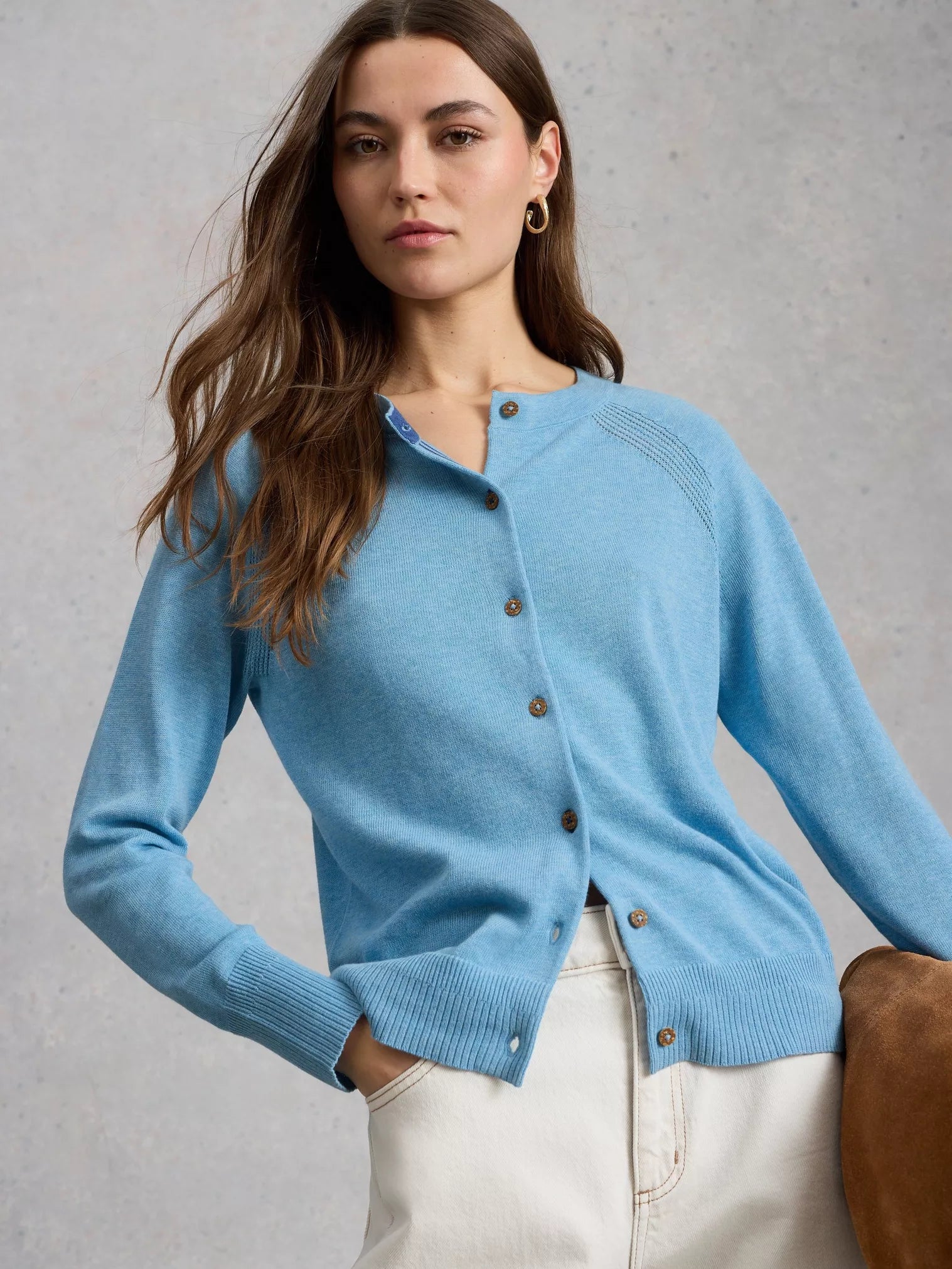 Woman wearing a light blue cardigan with brown buttons against a gray background