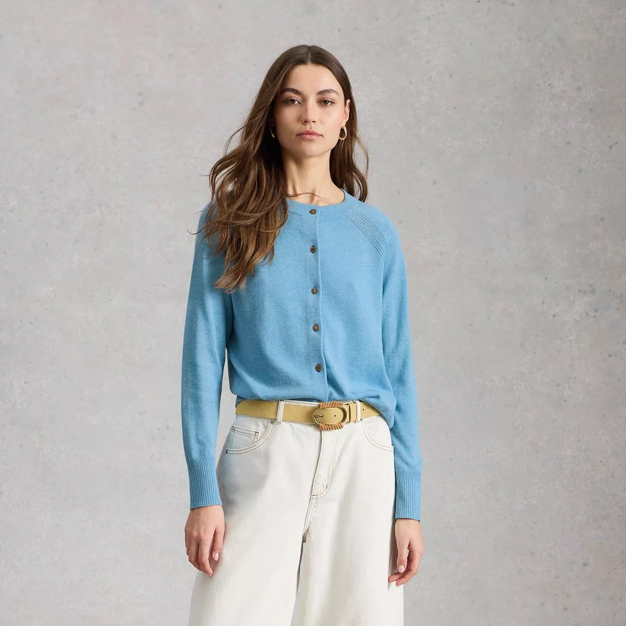 Woman wearing a blue shirt and white pants against a gray background