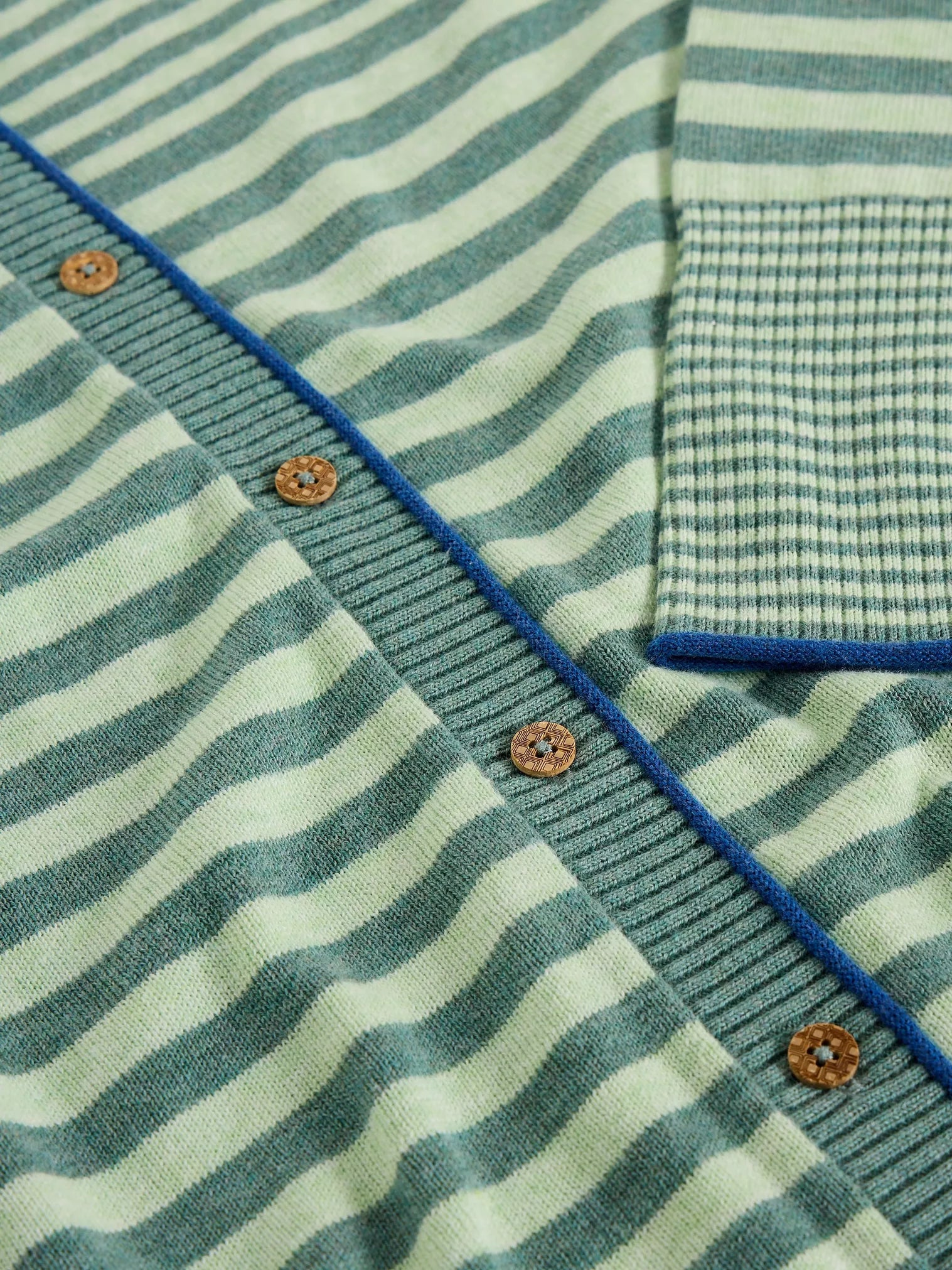 Close-up of a green and white striped sweater with blue trim and brown buttons.