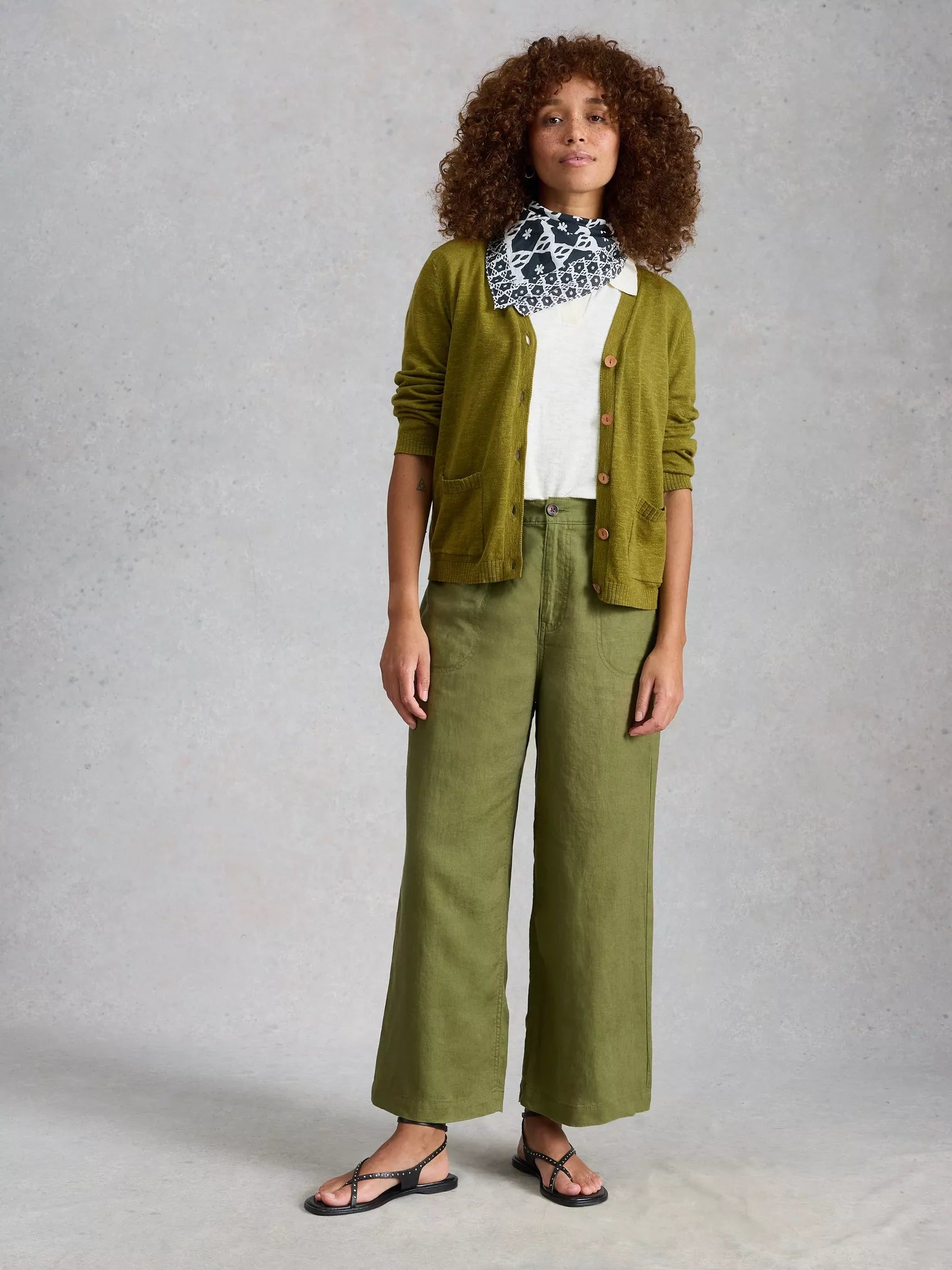 Woman wearing a green cardigan, white shirt, and green pants against a gray background