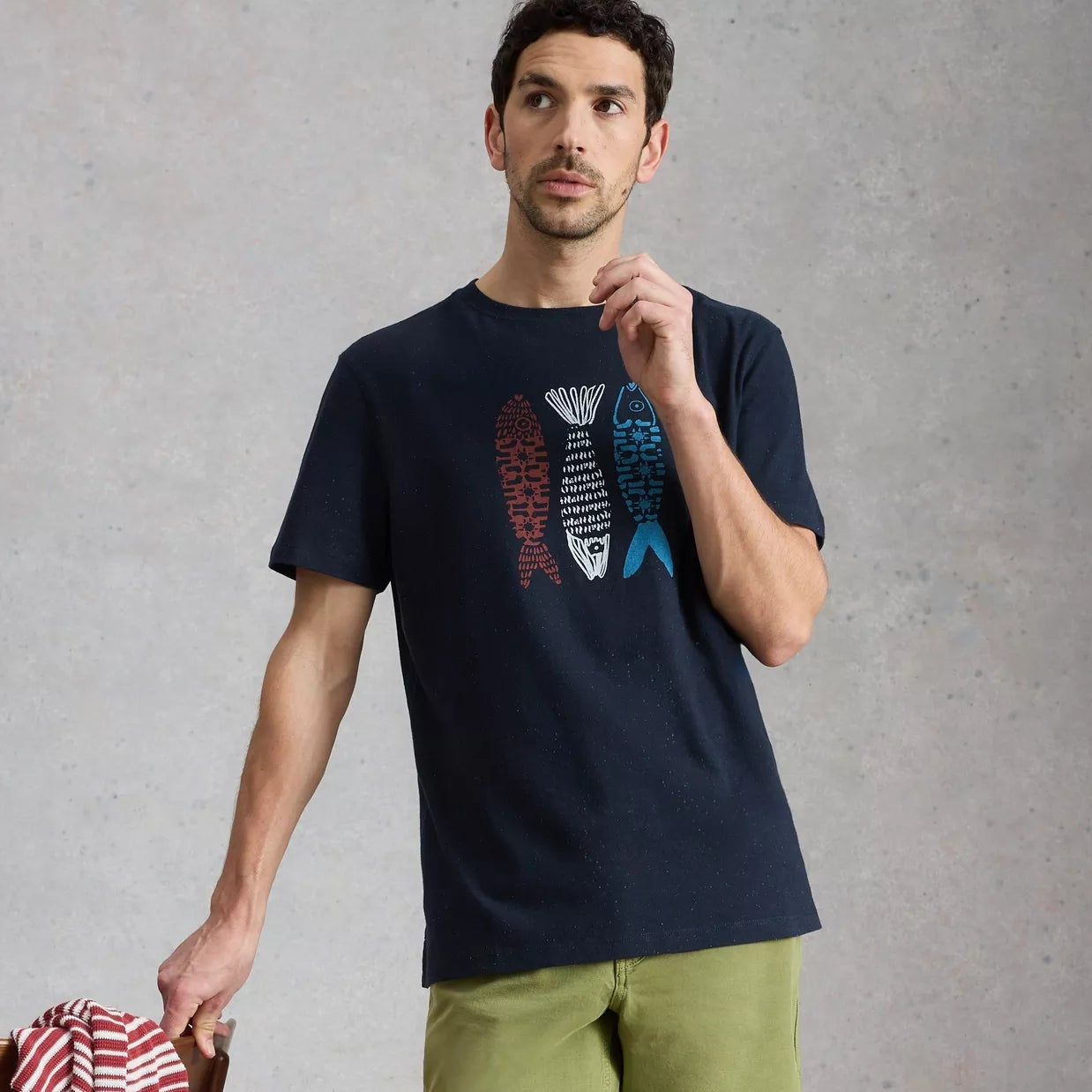 Man wearing a navy t-shirt with graphic design and green shorts, standing against a gray background.