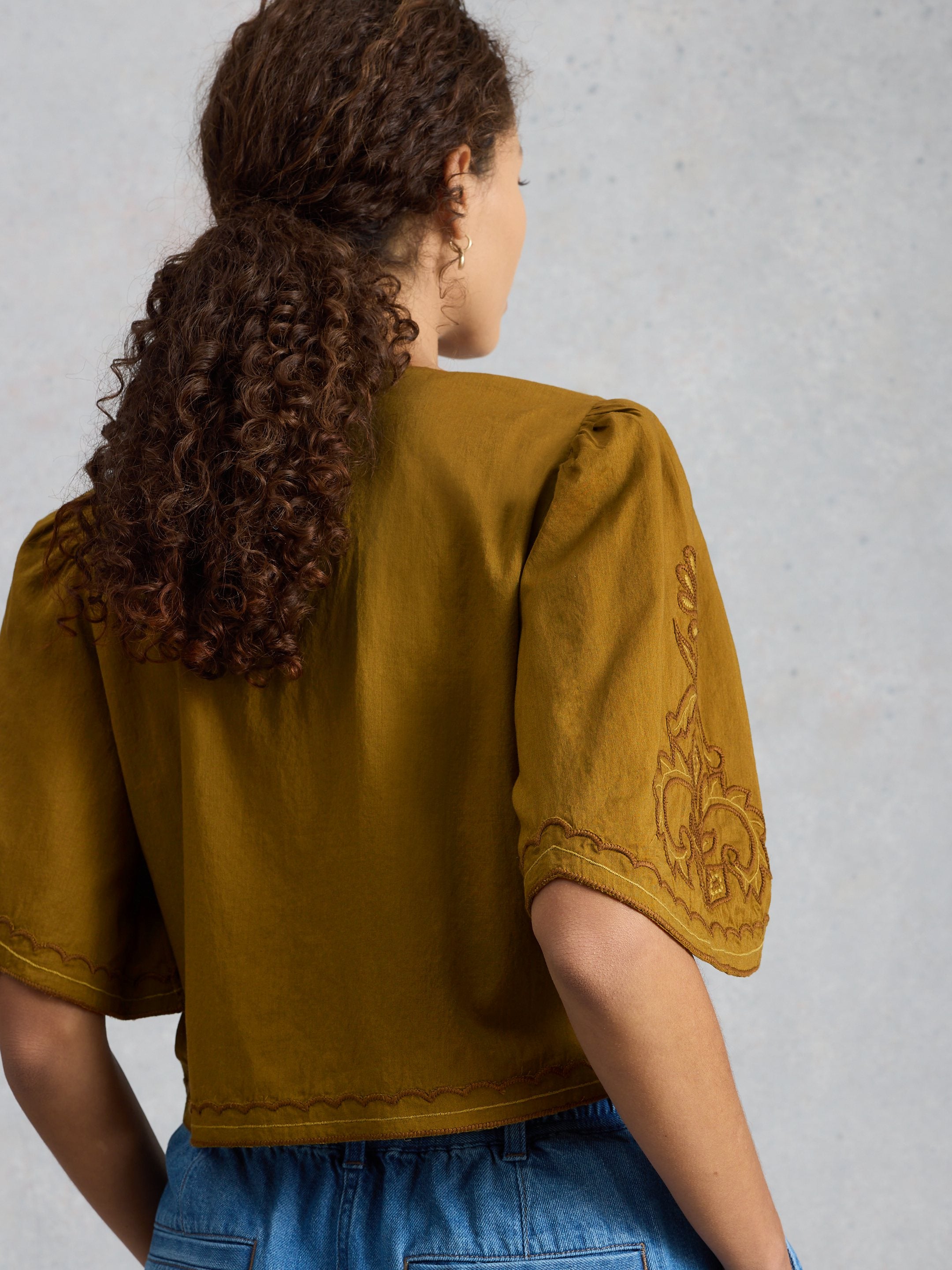Person wearing a mustard yellow top with floral embroidery on a plain background