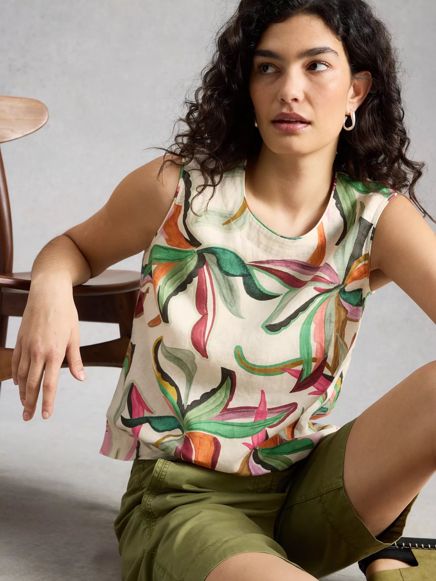 Woman wearing a sleeveless top with a colorful leaf pattern, sitting on a chair.