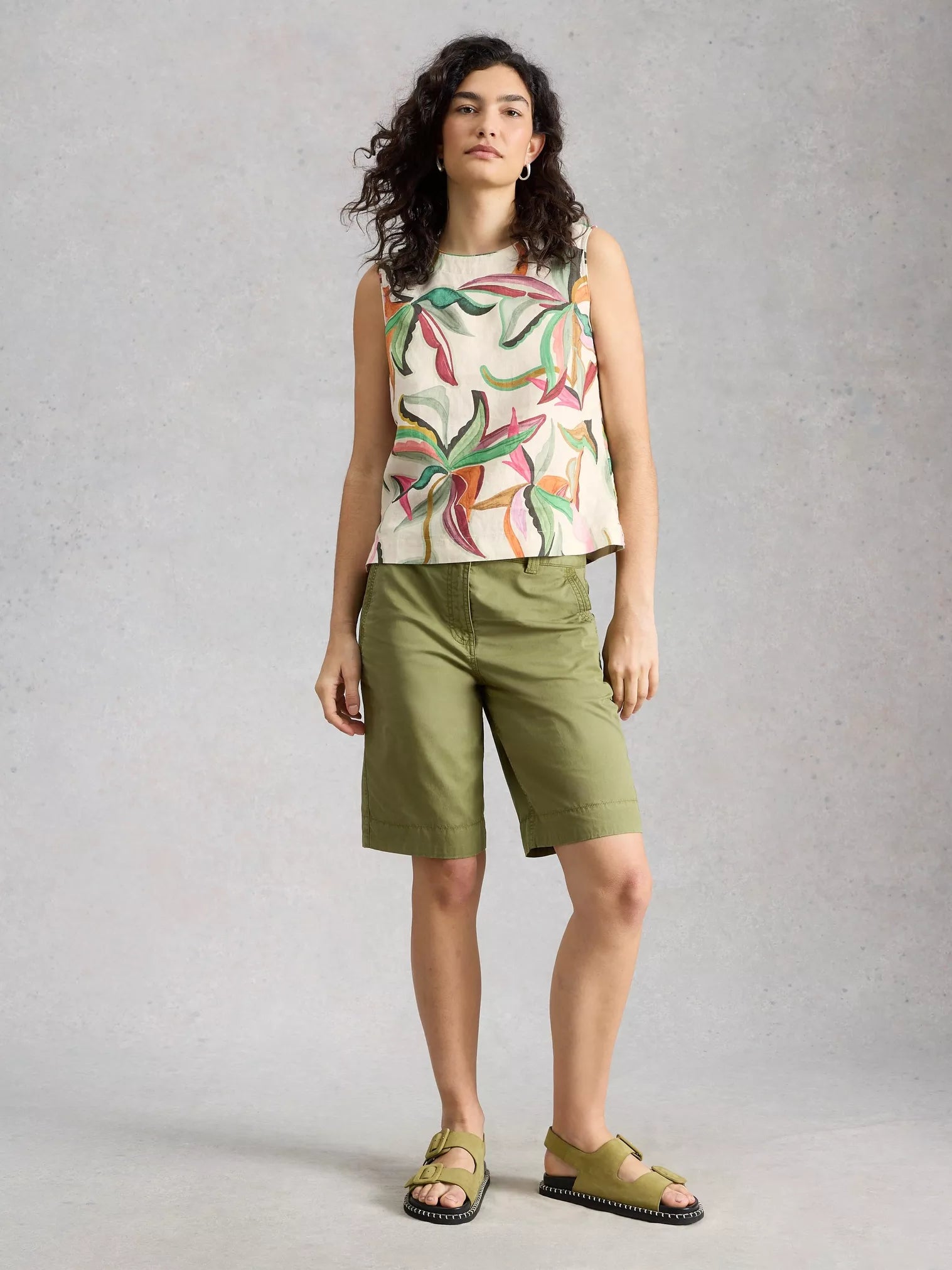 Woman wearing a sleeveless floral top and green shorts on a gray background