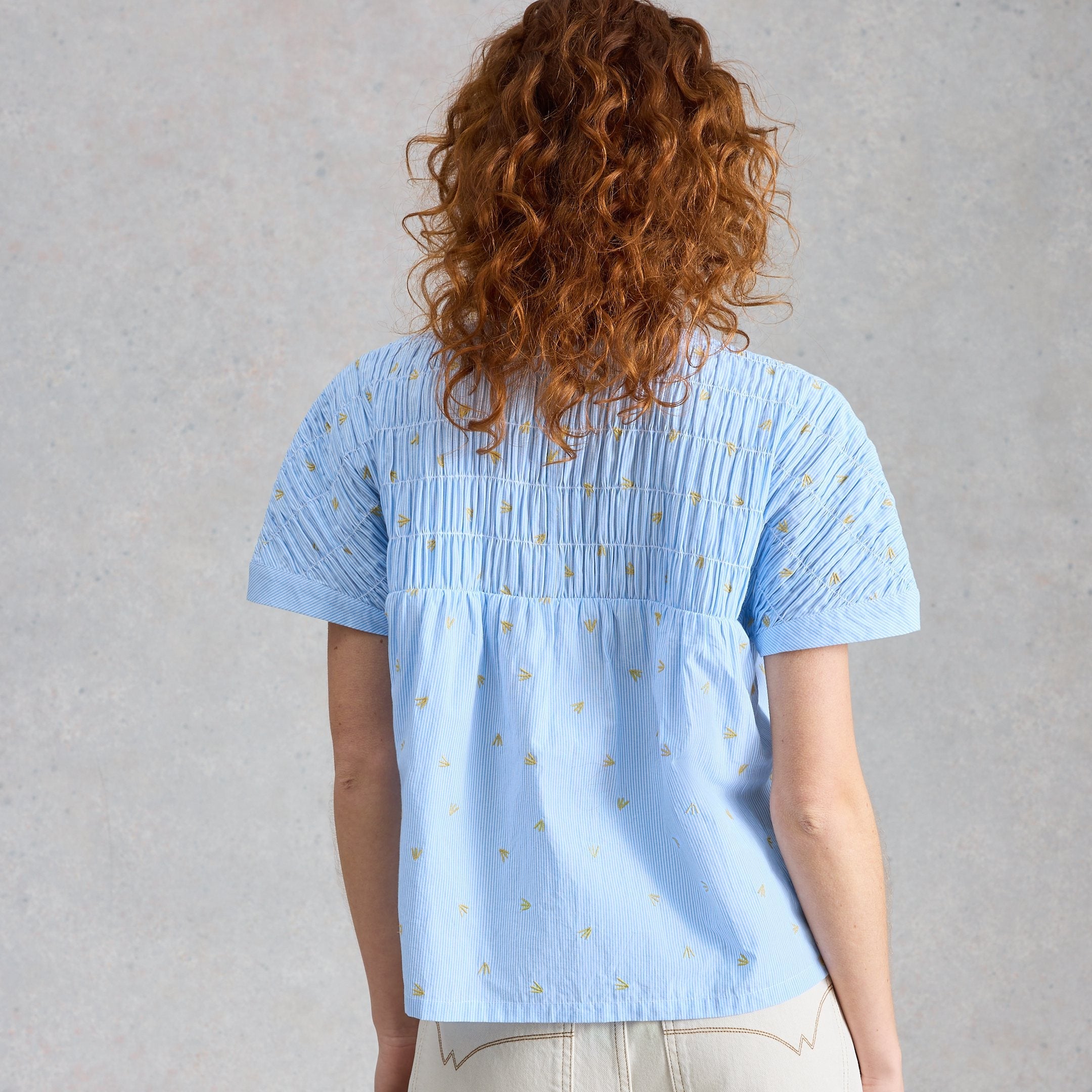 Person wearing a light blue patterned shirt and beige pants against a gray background