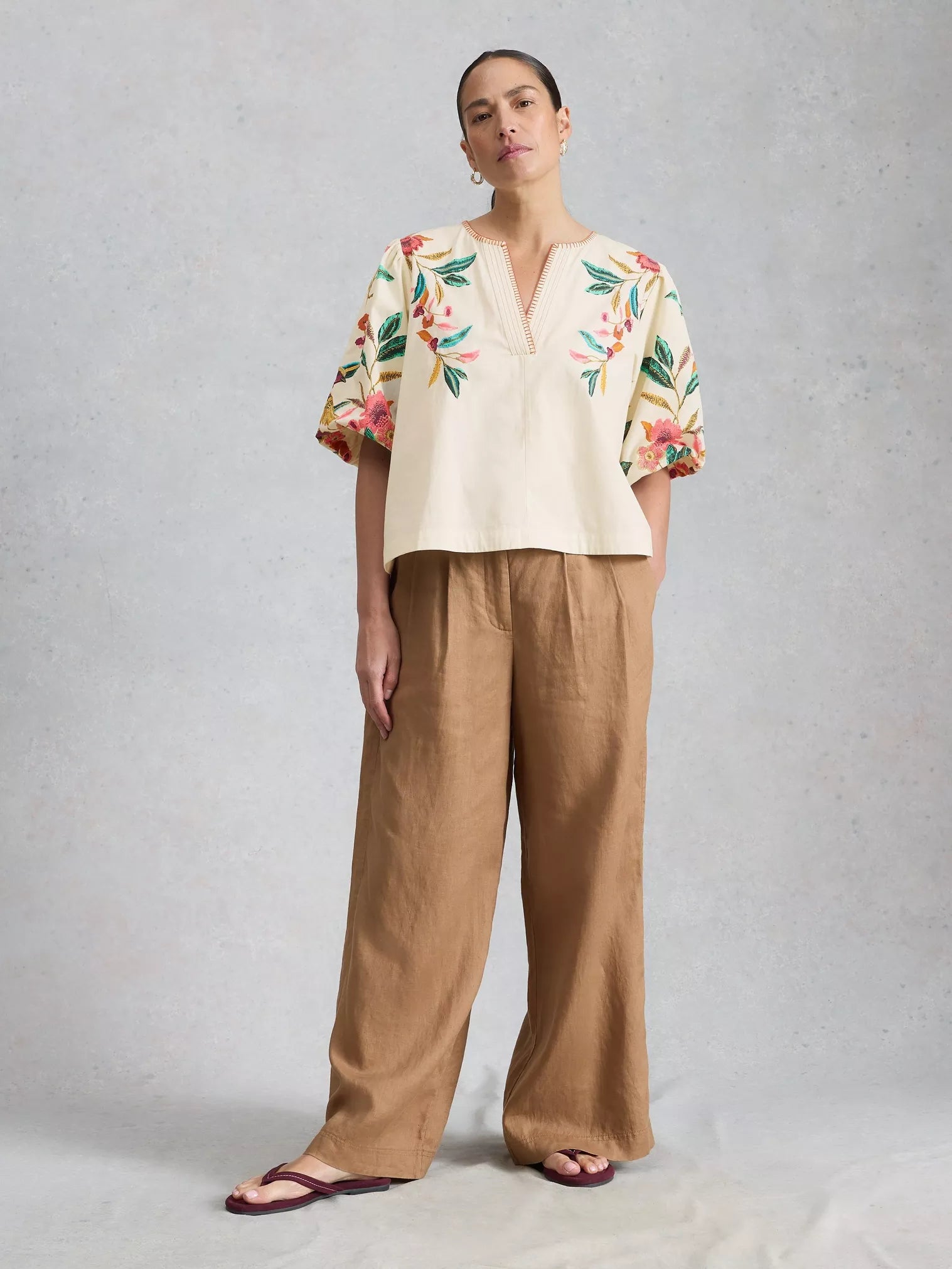Woman wearing a floral top and beige pants on a gray background