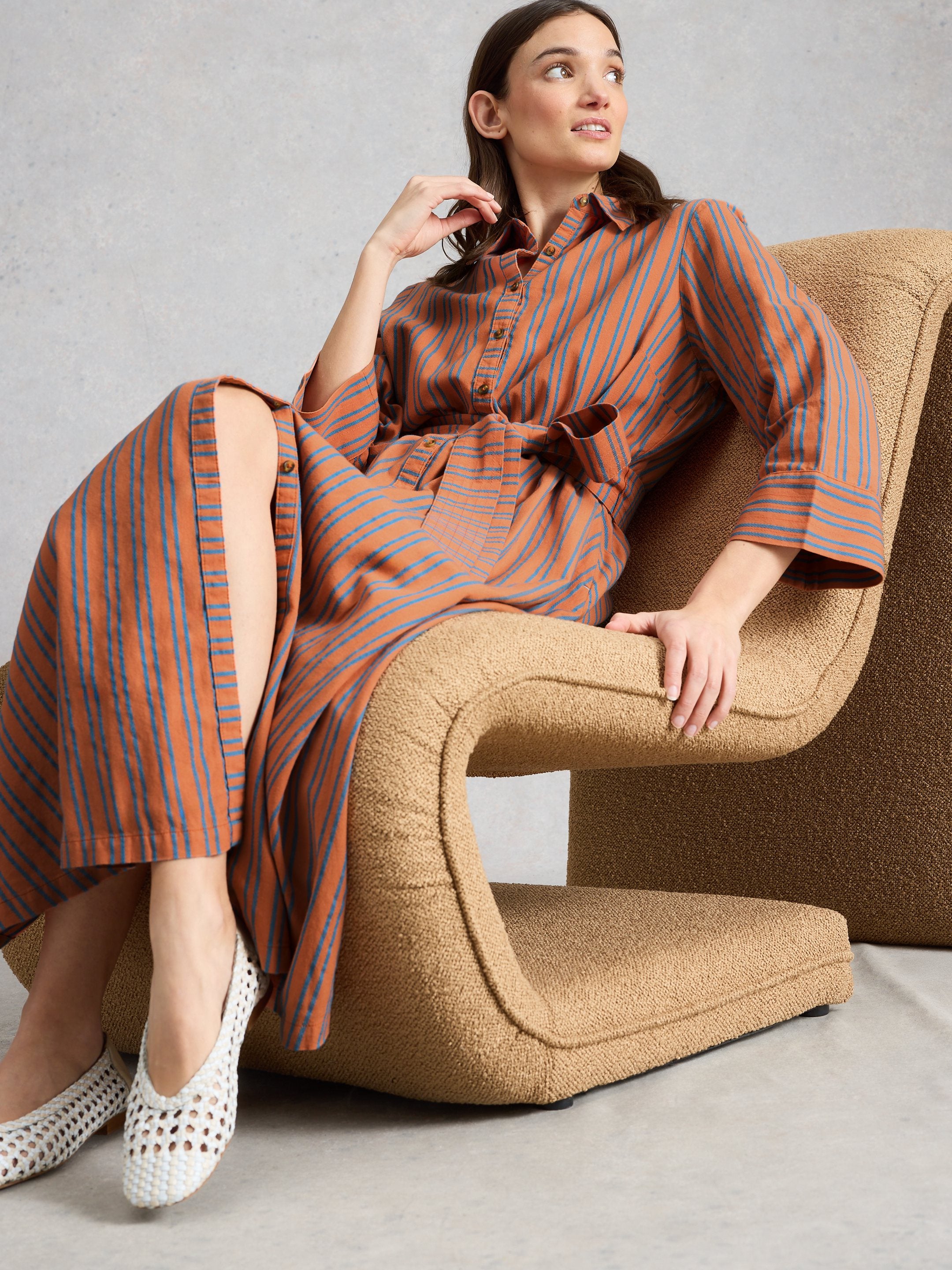 Woman in a striped dress sitting on a brown chair against a gray background