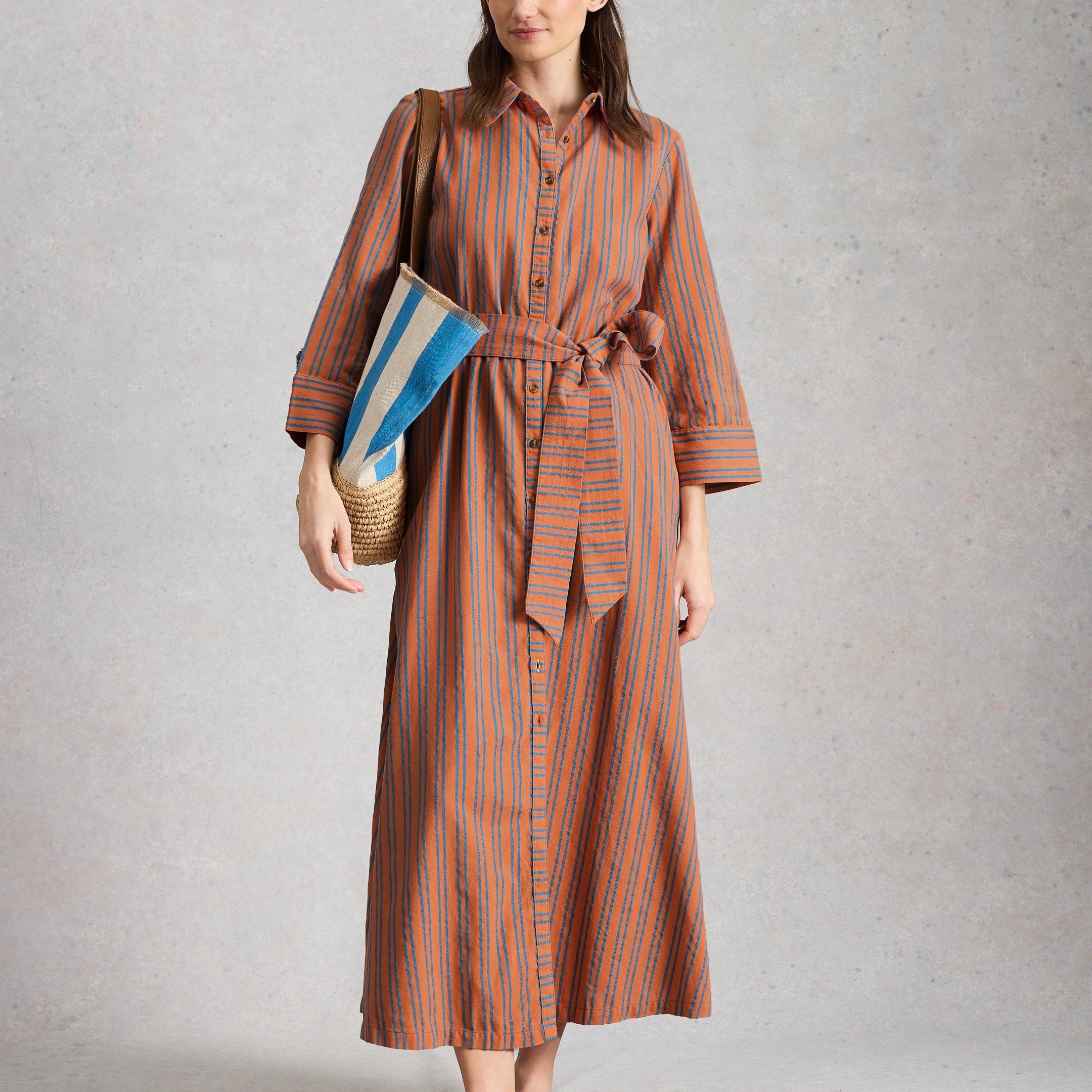 Woman wearing a striped dress holding a book against a plain background