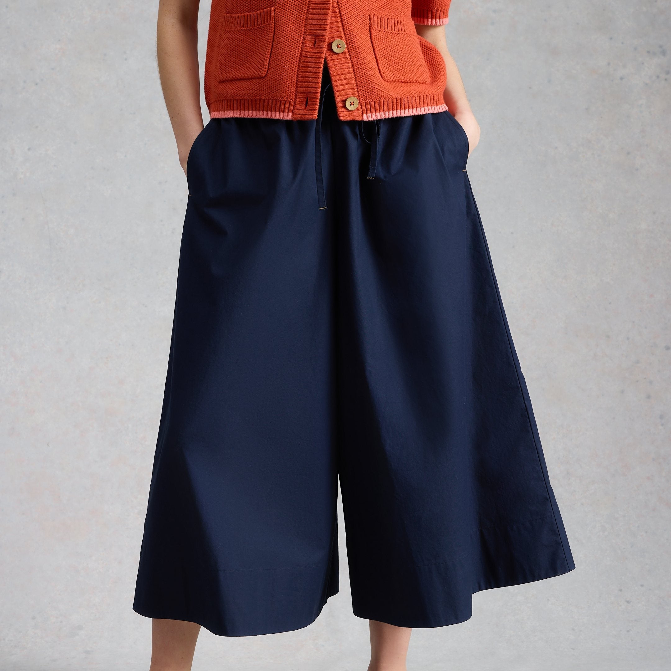 Person wearing a red cardigan and navy wide-leg pants on a gray background