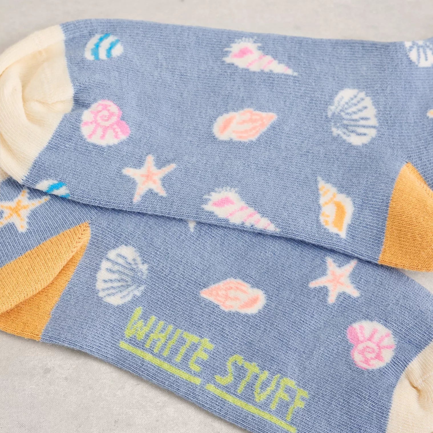 Pair of blue socks with shell and starfish pattern and 'White Stuff' branding on a light gray background.