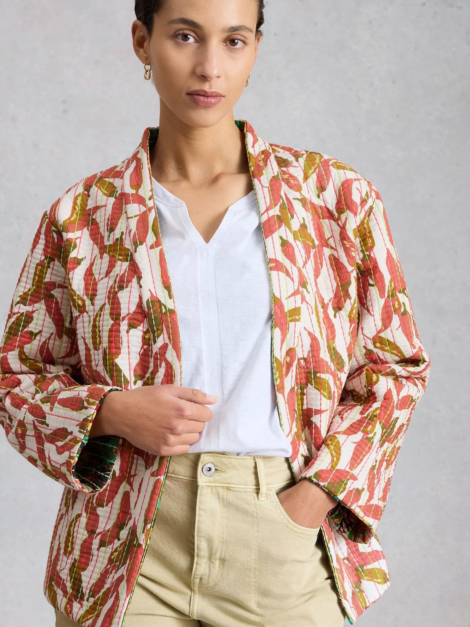 Person wearing a colorful patterned jacket over a white shirt and beige pants on a gray background