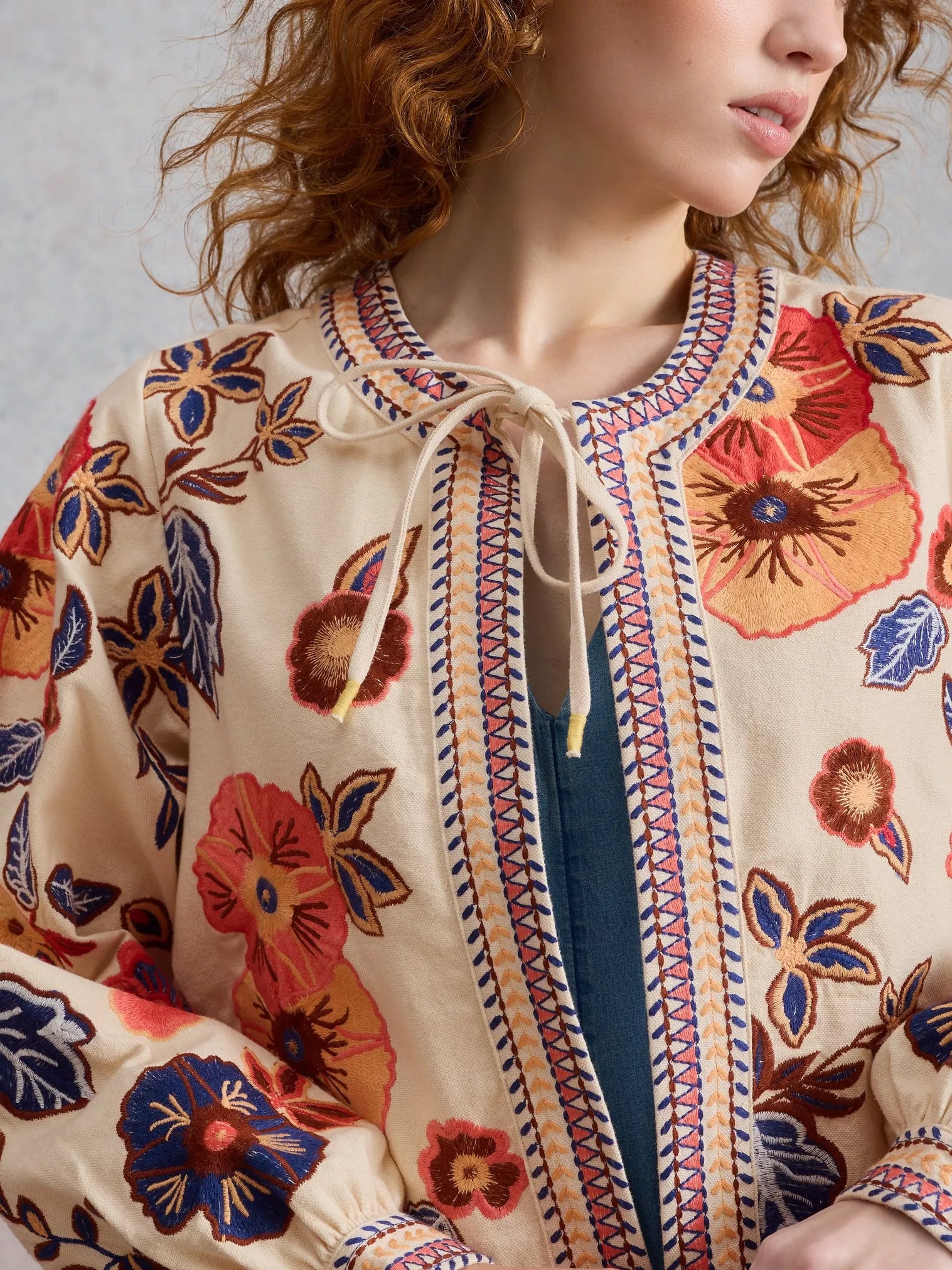 Woman wearing a floral embroidered jacket with a neutral background